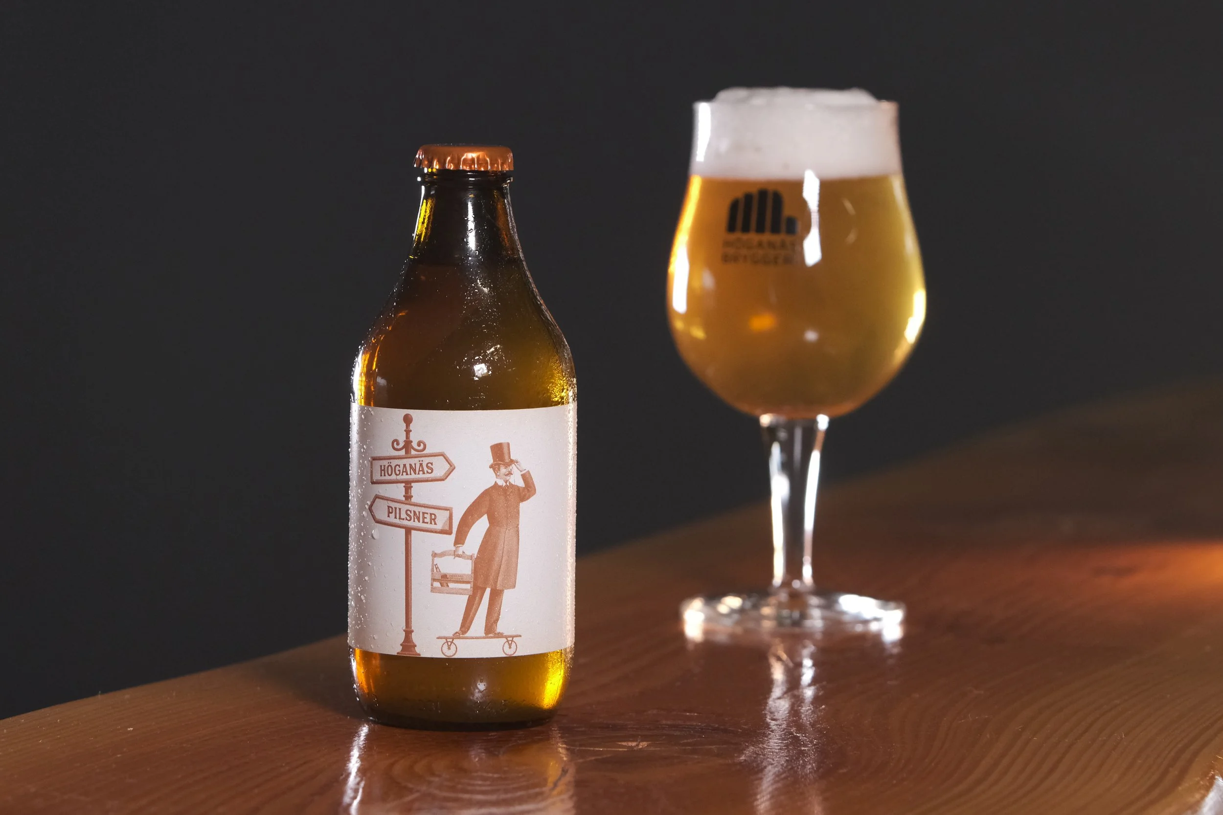 En ölflaska med etikett och ett glas öl med skum på toppen på en träbord.