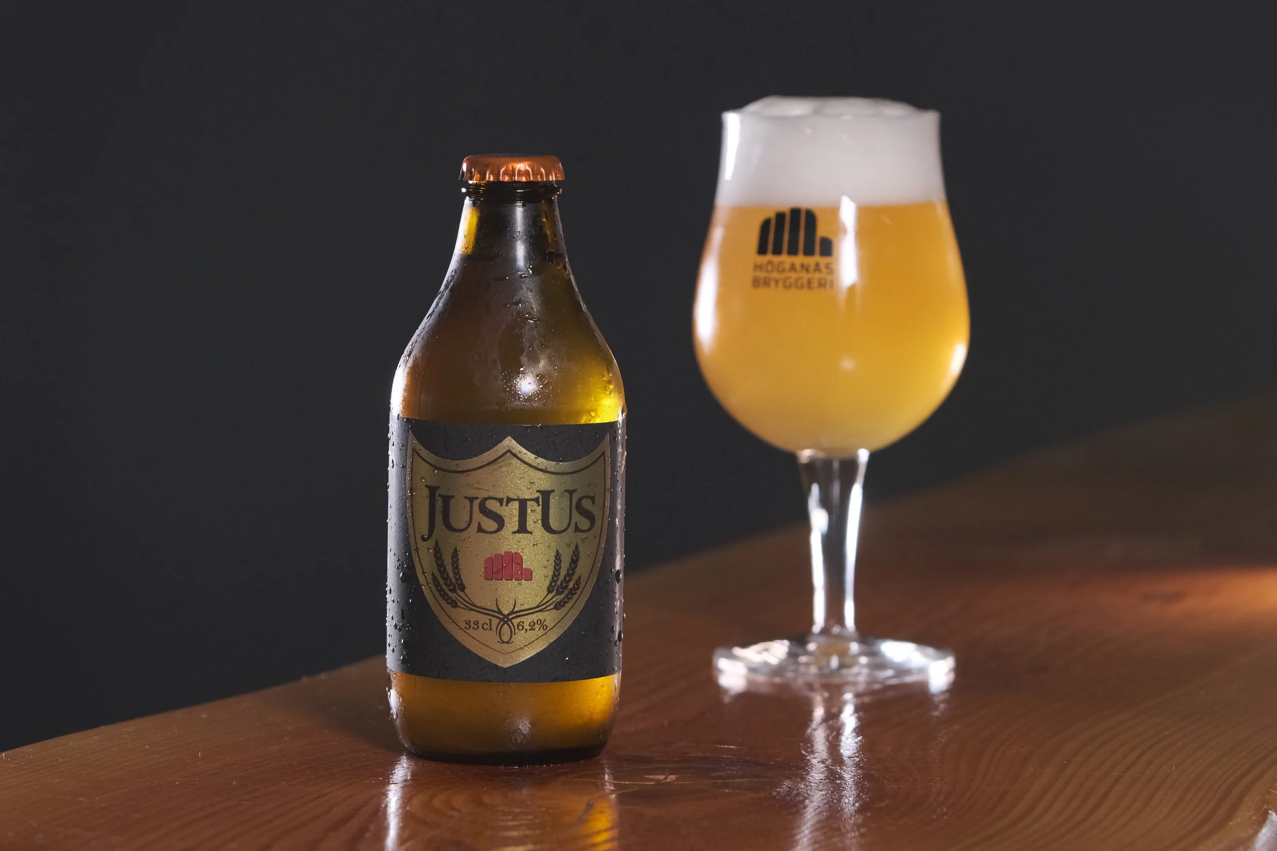 En öl i en glas och en ölflaska på ett träbord mot en mörk bakgrund.
