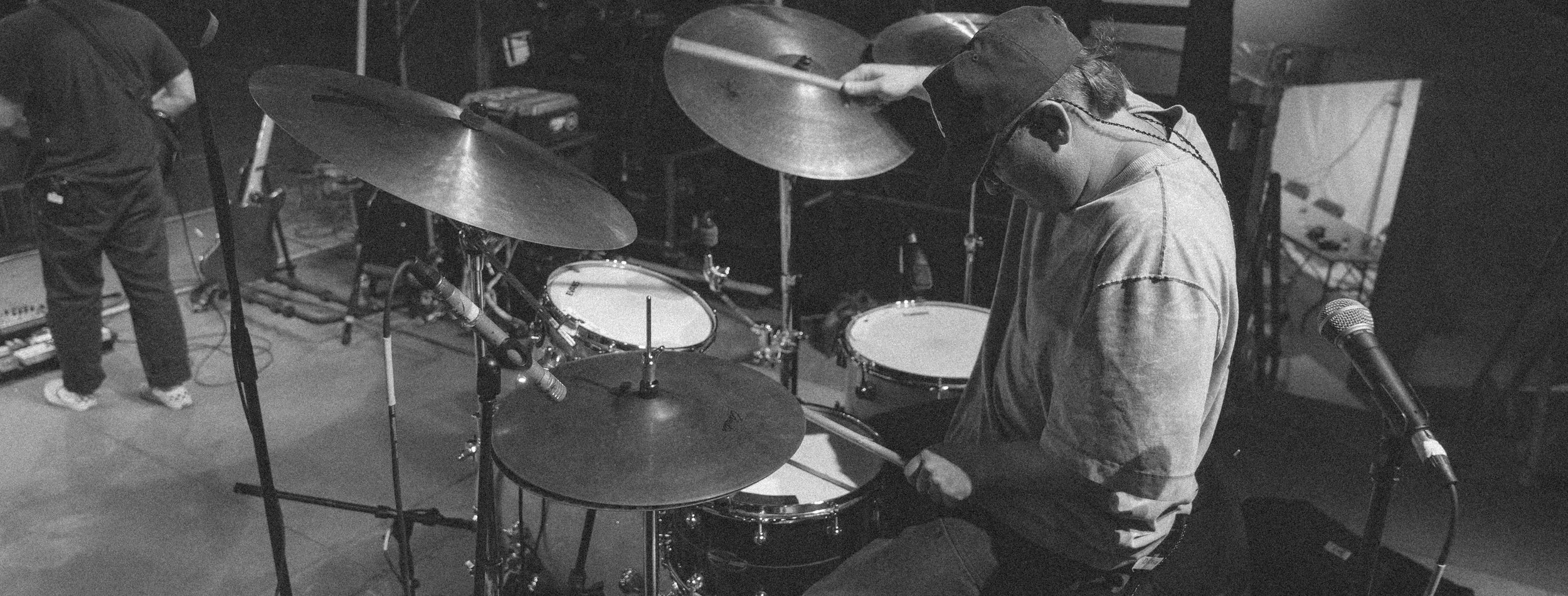 A person playing the drums in a music studio, with a microphone set up nearby.