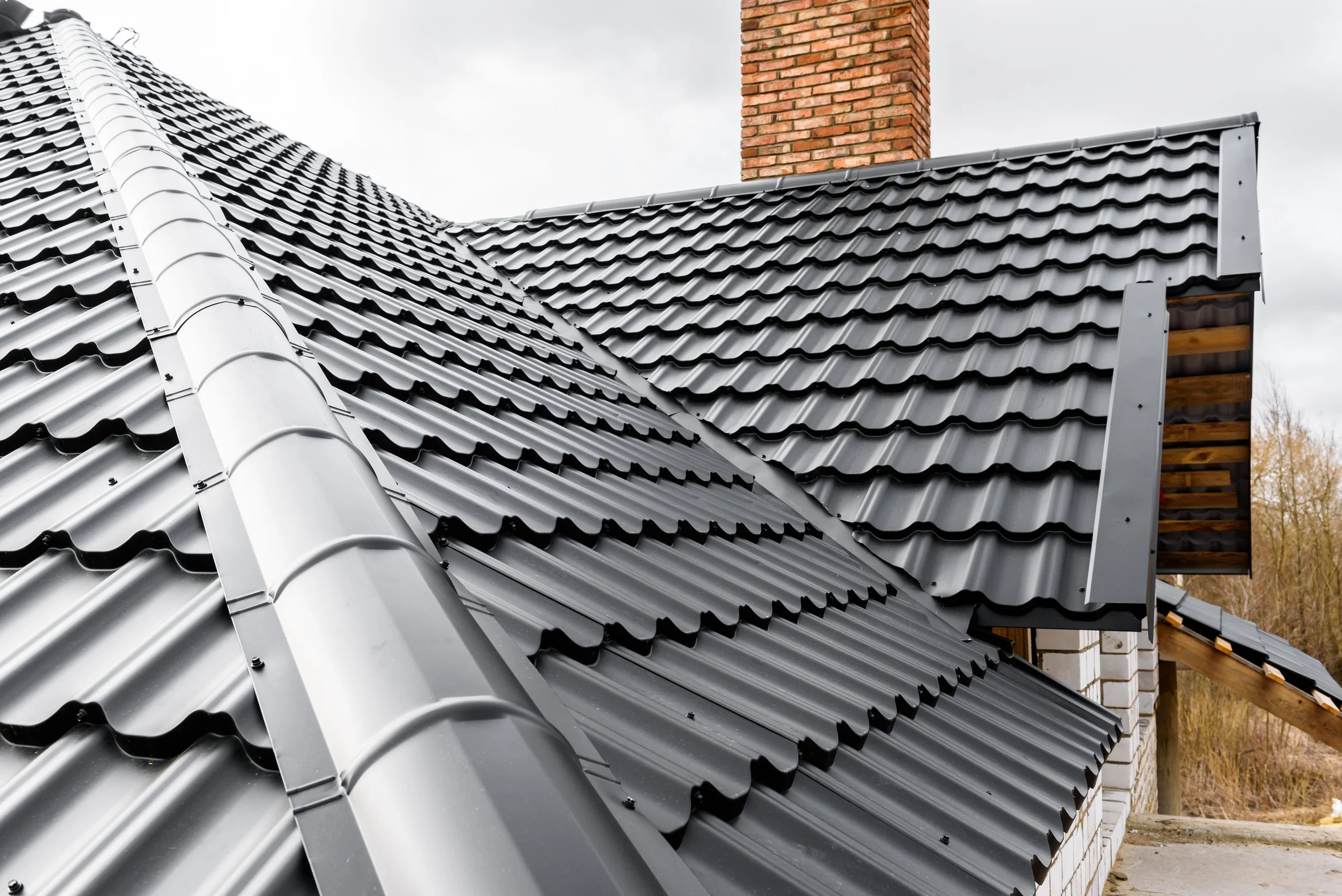 Metal roofing on a house under construction, with a brick chimney in the background.