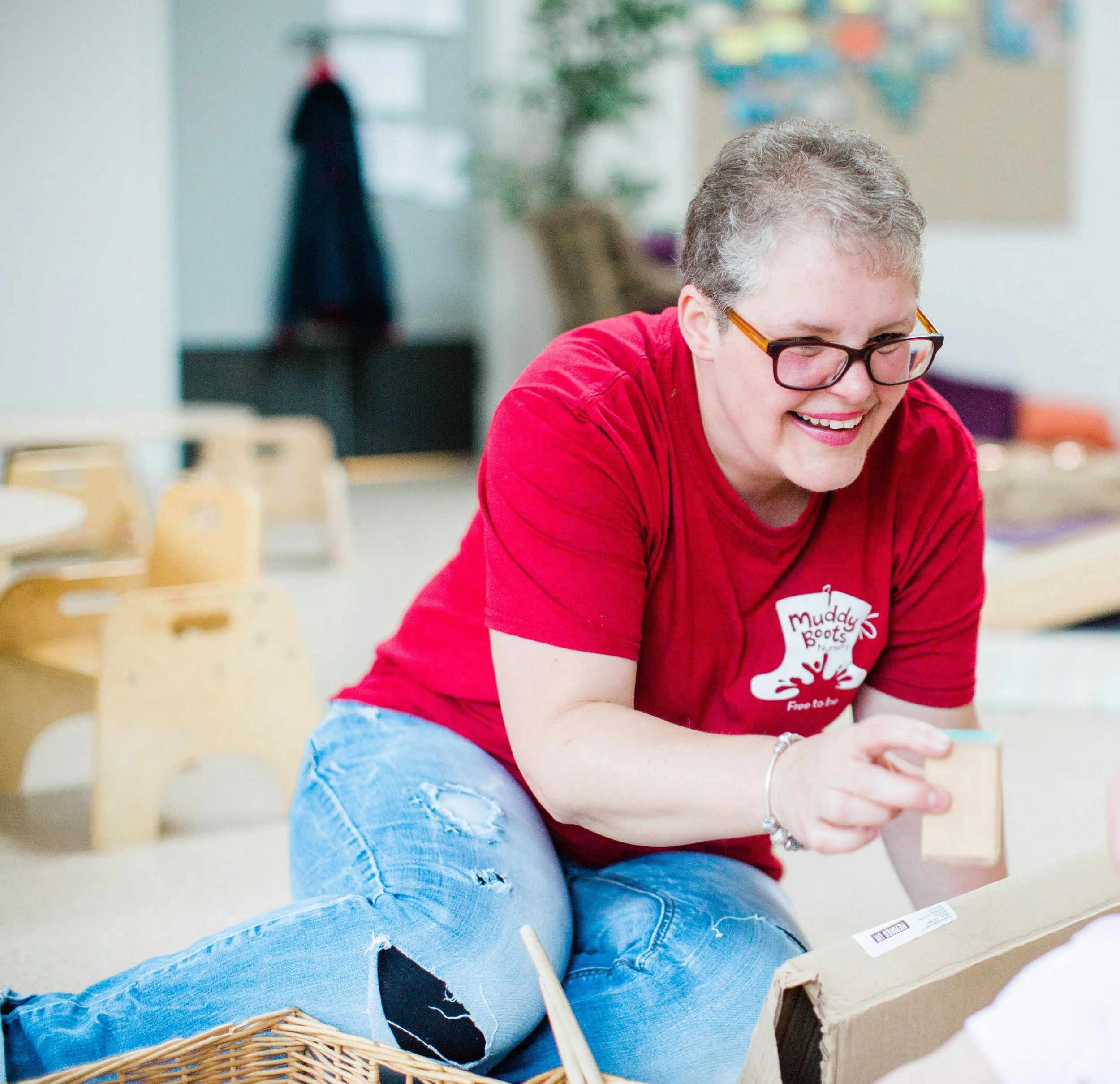 Person wearing a red shirt playing with a child, holding building block, smiling and looking down, indoors