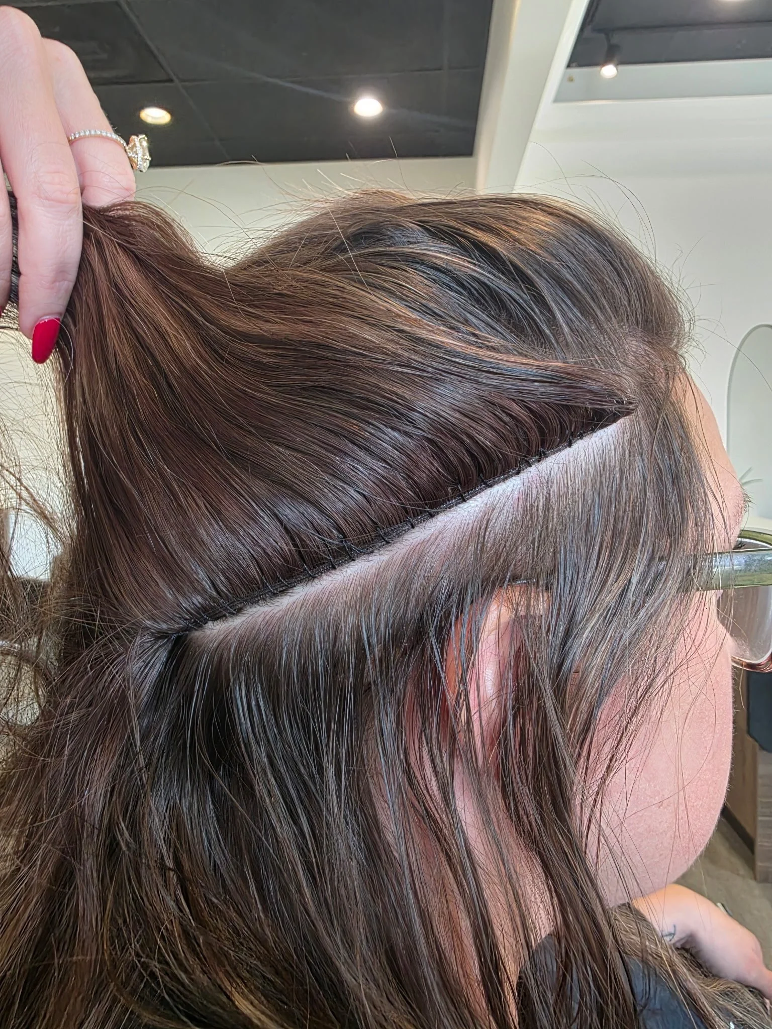 Close-up of a woman's head showing freshly highlighted, wet, brown hair with a clean, straight parting, in a salon setting.