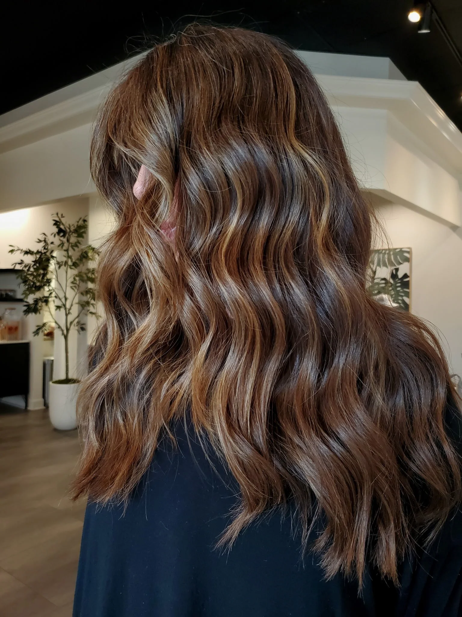 Wavy brunette hair with blonde highlights on a person in a salon setting.