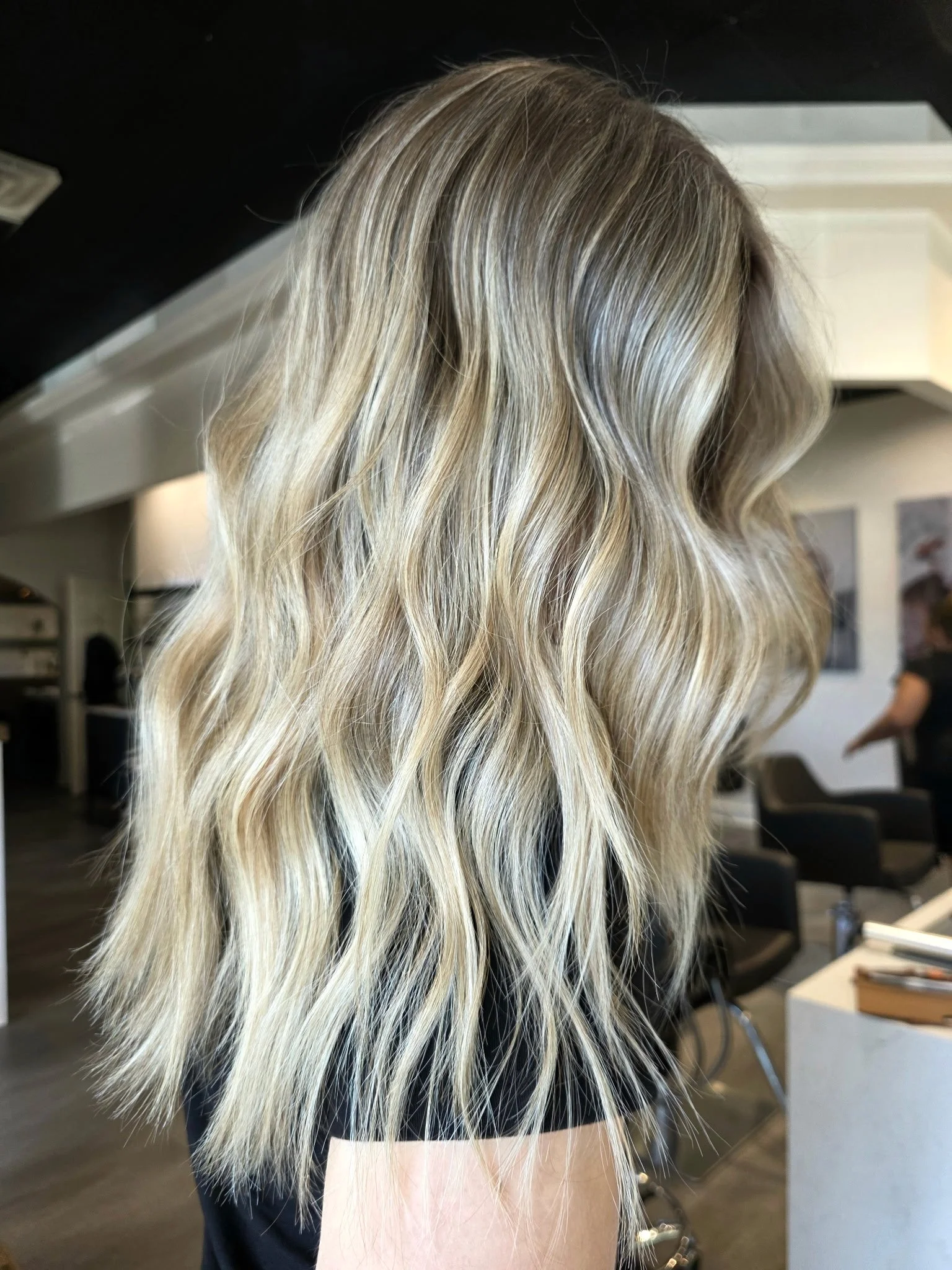 Blonde, wavy hair with highlights on a woman in a salon or similar setting.