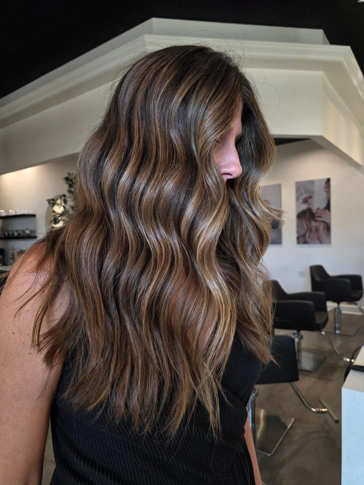 Side view of a woman with long, wavy, light brown hair in a salon setting.