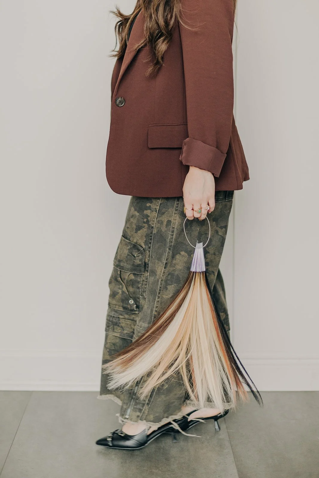 Person holding a bundle of hair color samples in various shades, wearing a watch and a beige top.
