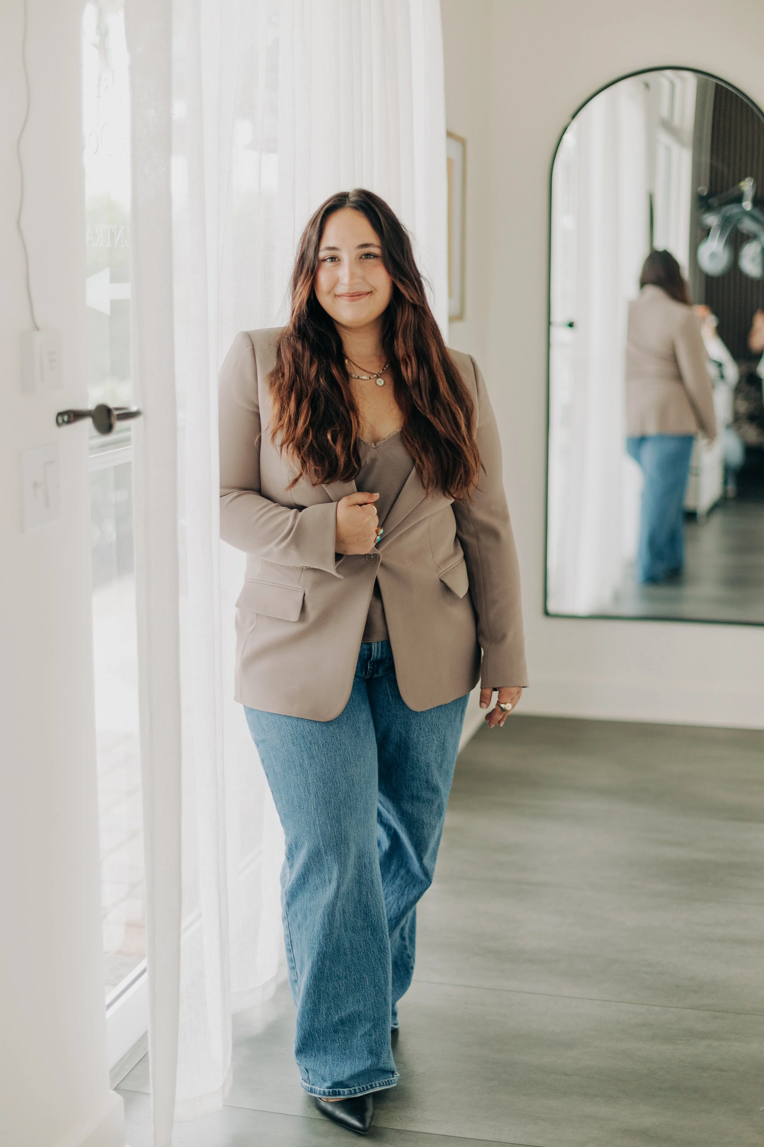 A young woman with red hair and tattoos smiling at the camera while standing in a modern interior.