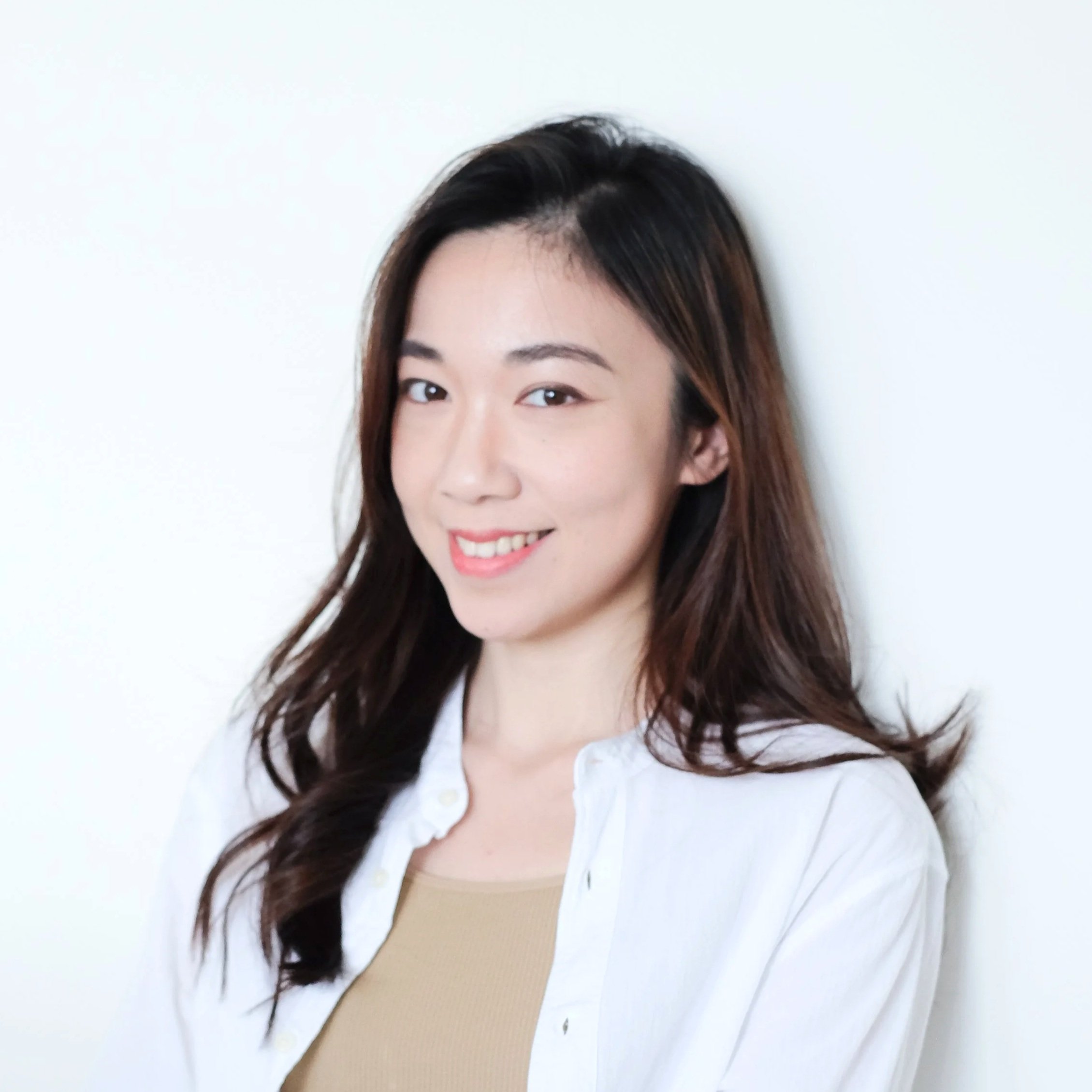 A woman with long dark hair and fair skin smiling in front of a plain white background.