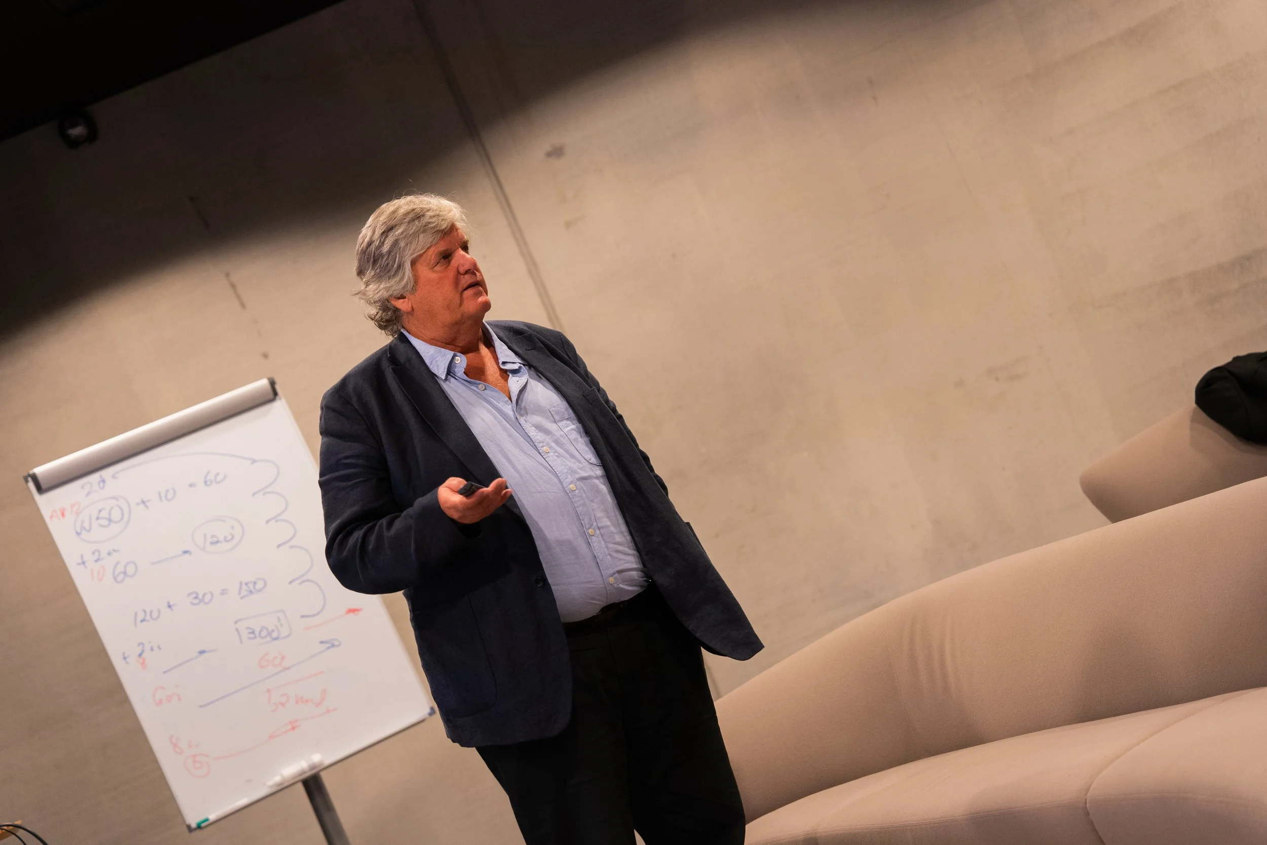 man med grått hår foreleser foran en flipover.
