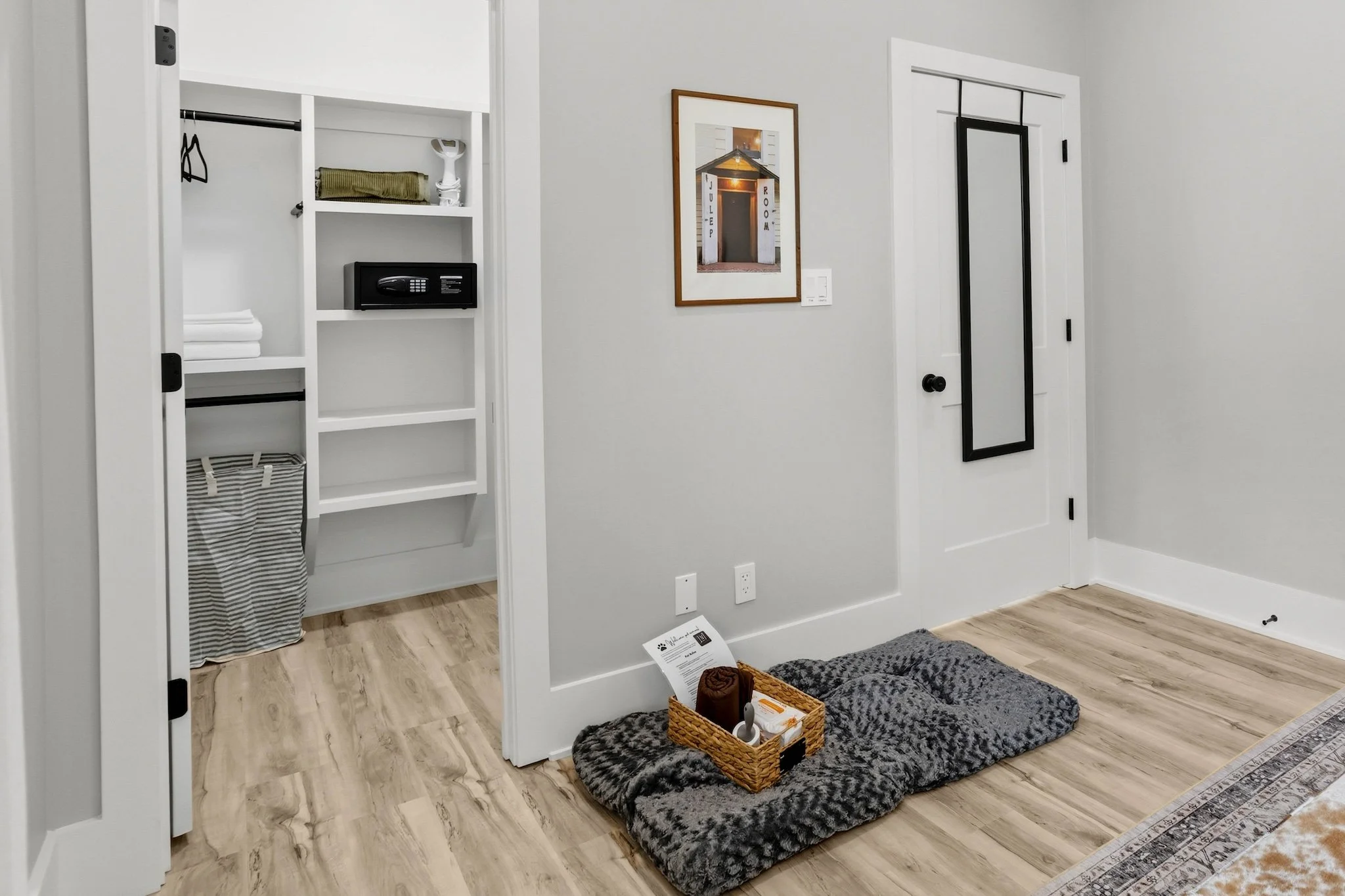 Entryway with pet bed, basket, and framed mirror, with an open closet and framed picture on the wall.
