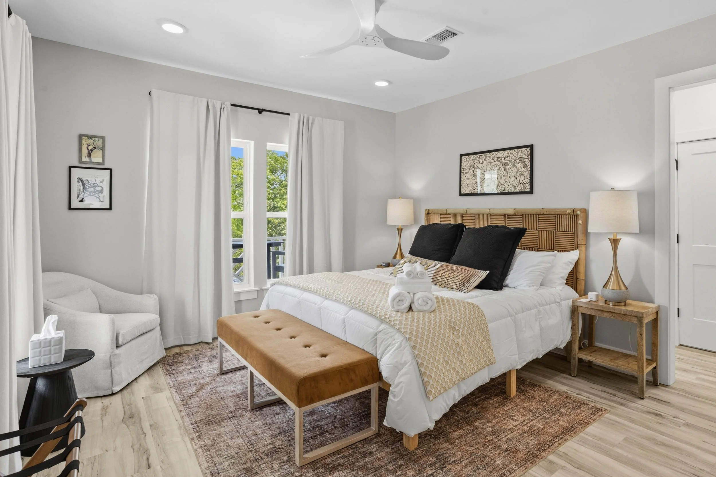 A bedroom with a bed, nightstands, lamps, a chair, and a window with white curtains, in a modern, minimalist style.