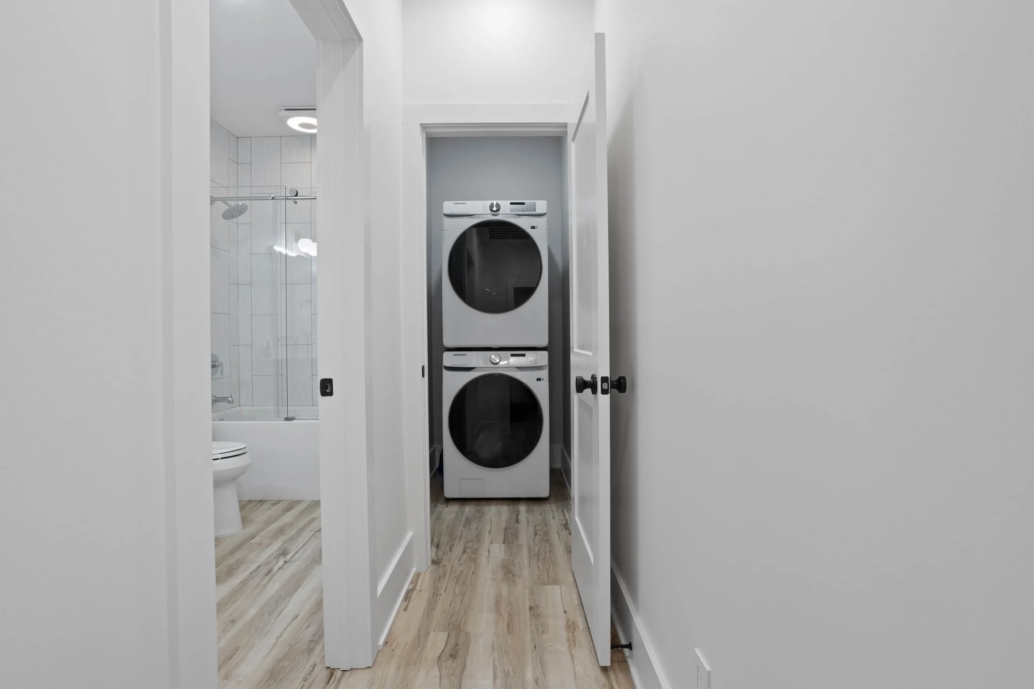 Laundry area with stacked washer and dryer behind a partially open door, adjacent to a bathroom with a toilet and shower.