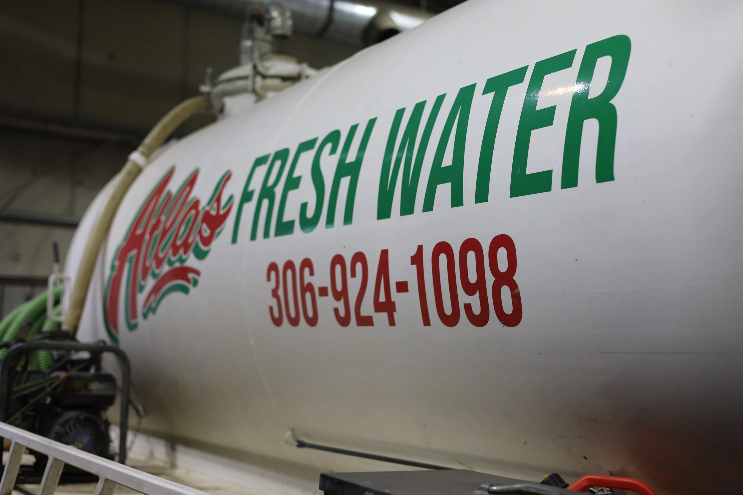 Atlas water delivery truck supplying fresh water to a construction site trailer for showers and toilets.