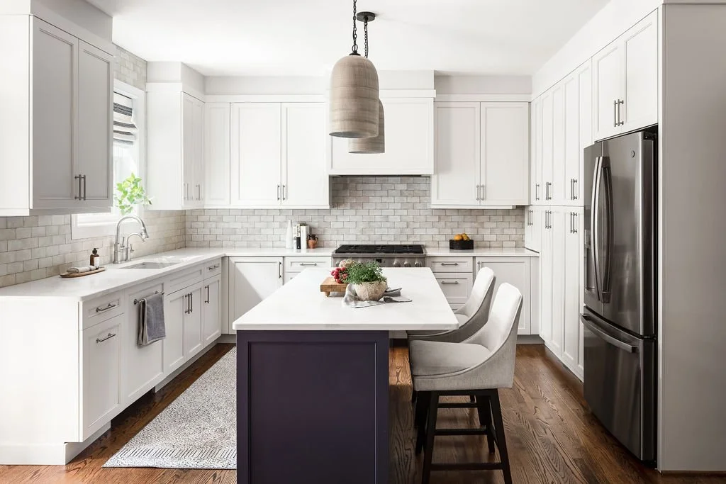 Modern white kitchen with a center island, stainless steel refrigerator, white cabinets, subway tile backsplash, and pendant lighting.