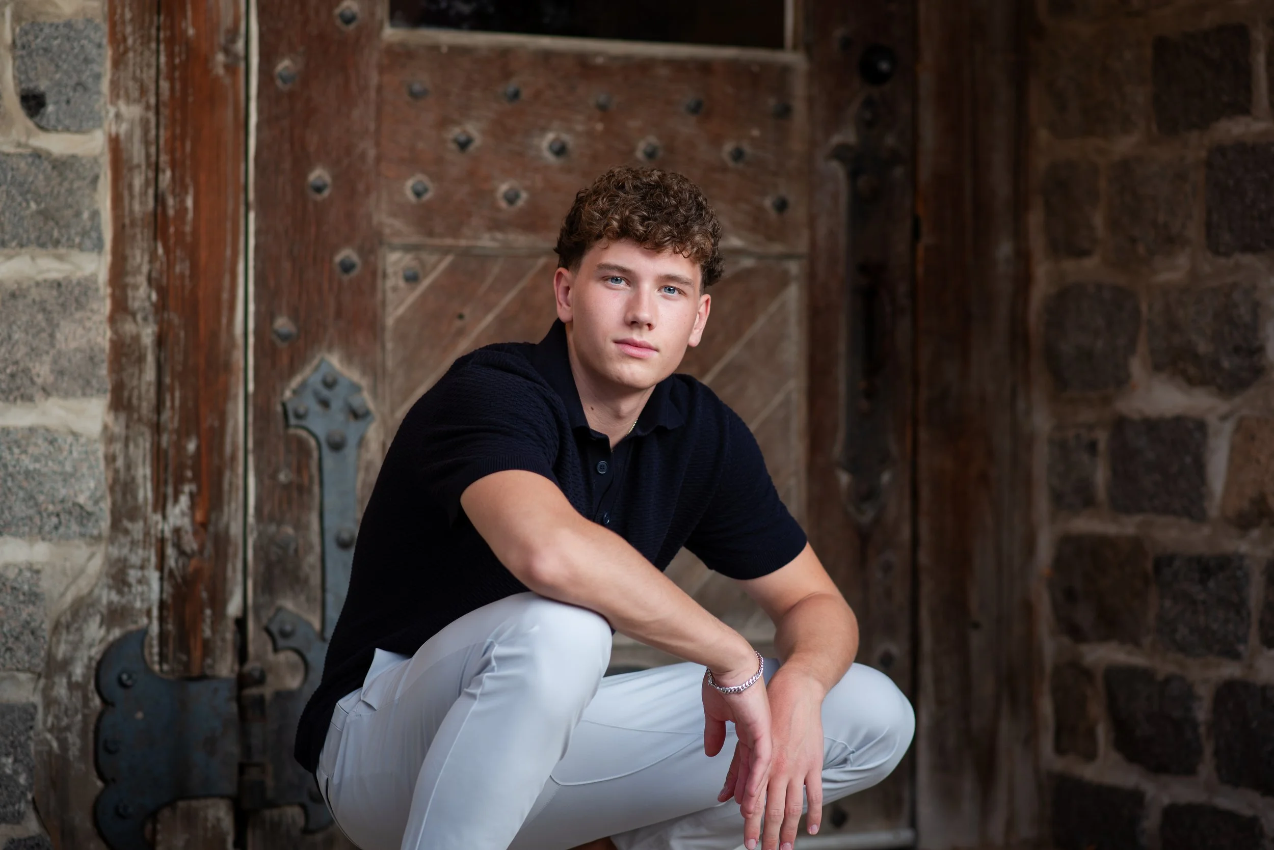 senior boy squatting in front of a door