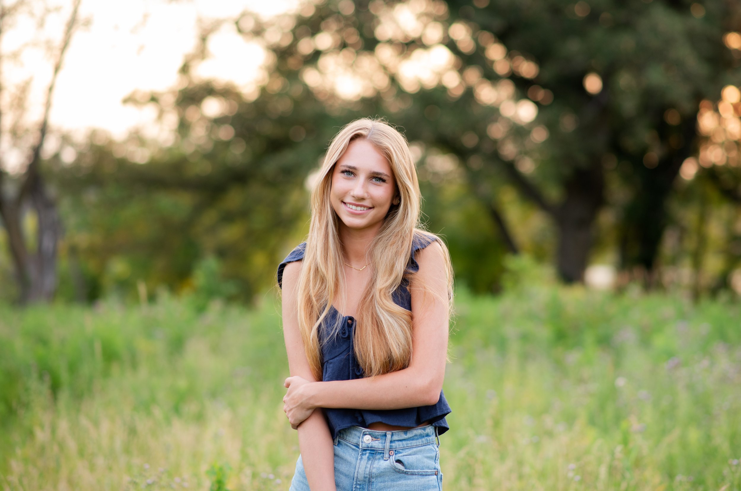 senior girl standing in field of flowers with sunset behind her at senior photo session in Chanhassen, MN