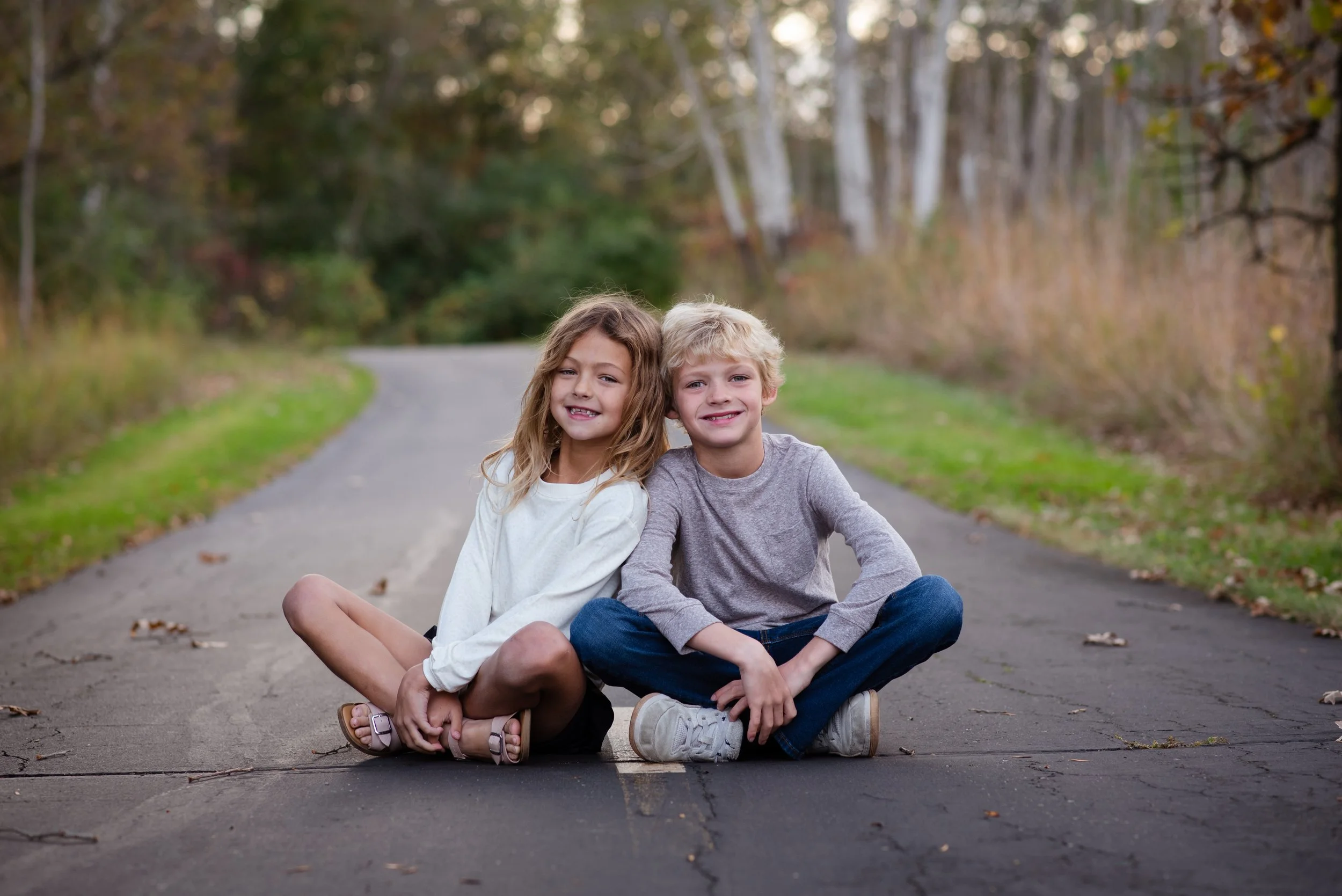 brother and sister sitting on path next to each other smiling