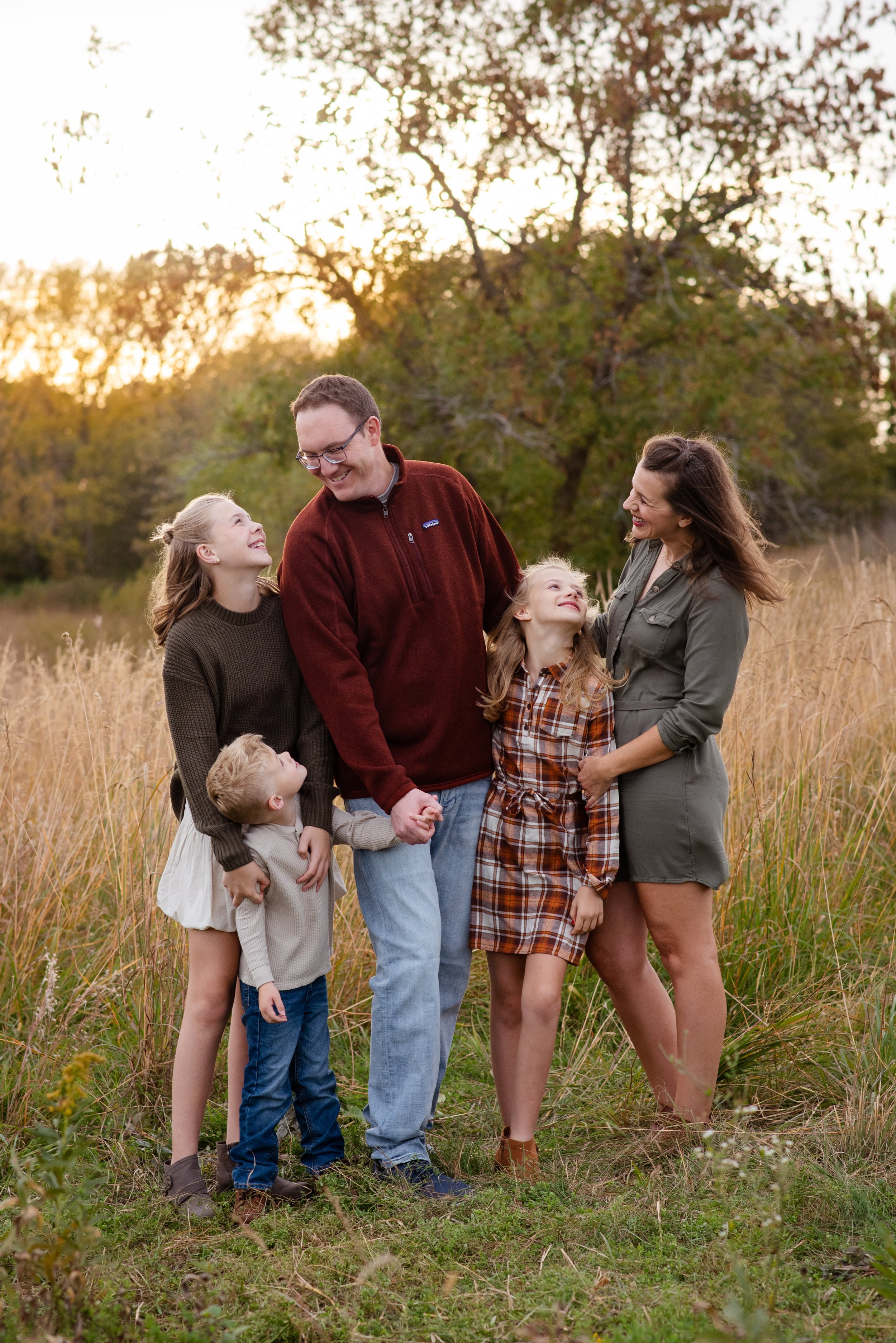 family gathered together in front of tree and sunset smiling and holding hands for outdoor family photo session at Lowry Nature Center in Victoria, MN