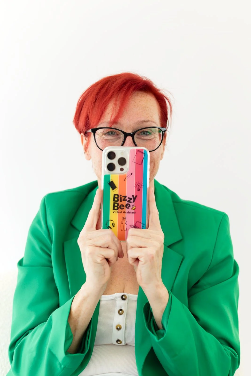 Woman with red hair and glasses taking a selfie with her phone, which has a colorful case that reads 'Bizzy Bee Virtual Assistant.'