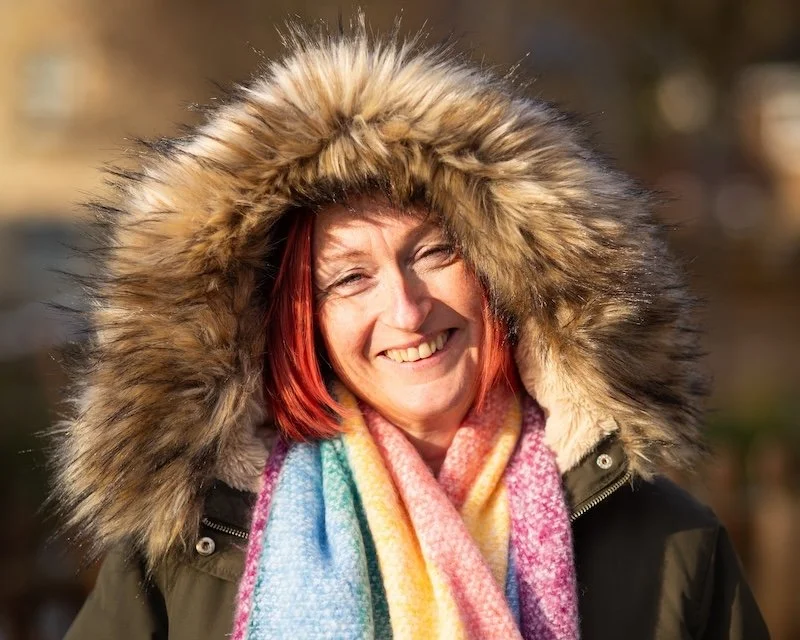 Erin, owner of BizzyBee Virtual & Social Assistant Services, smiling outdoors in a fur-lined hooded coat and colourful scarf.