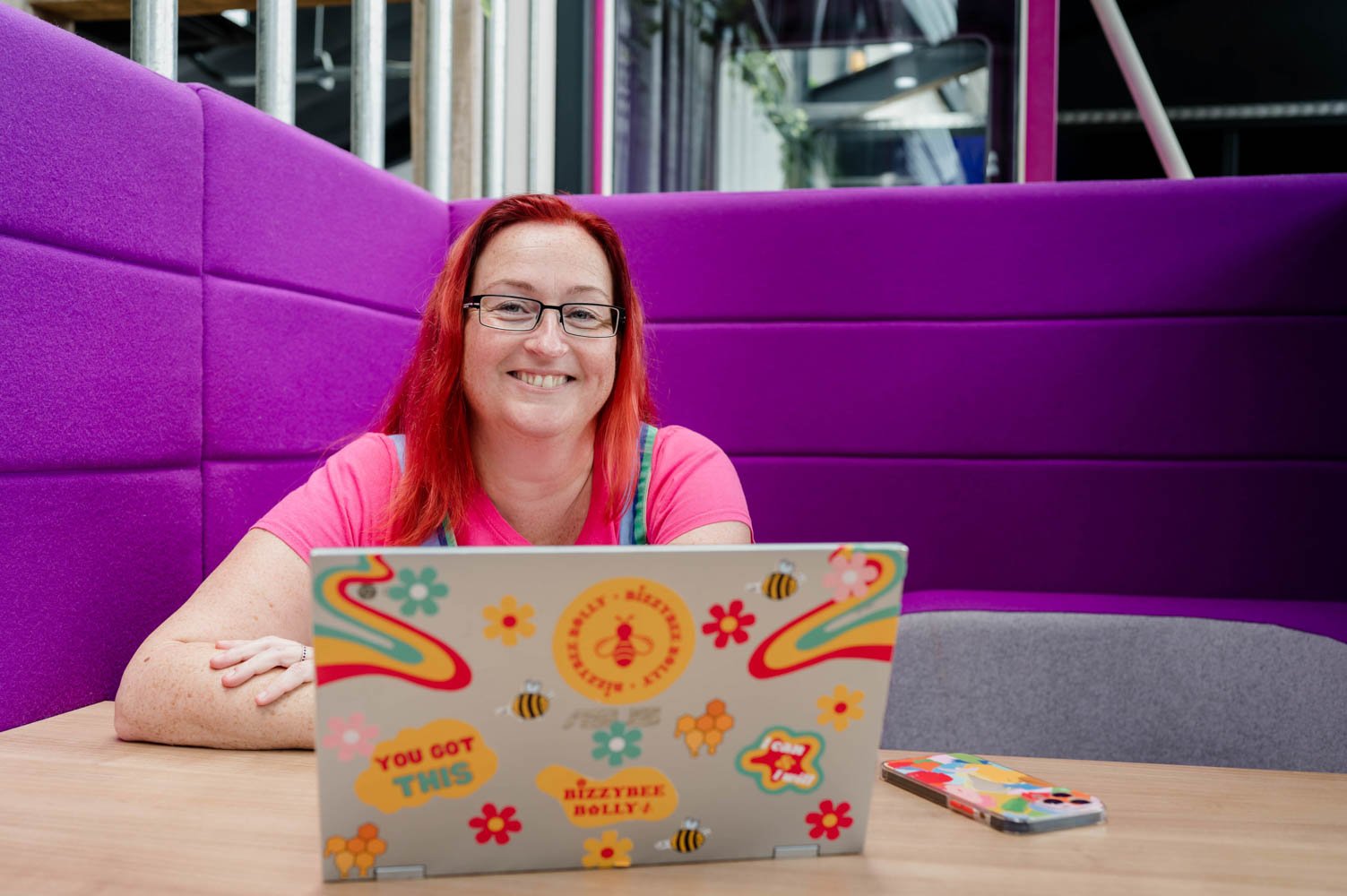 Erin, owner of BizzyBee, smiling at a laptop in a colourful workspace, showing a friendly and approachable virtual assistant at work.