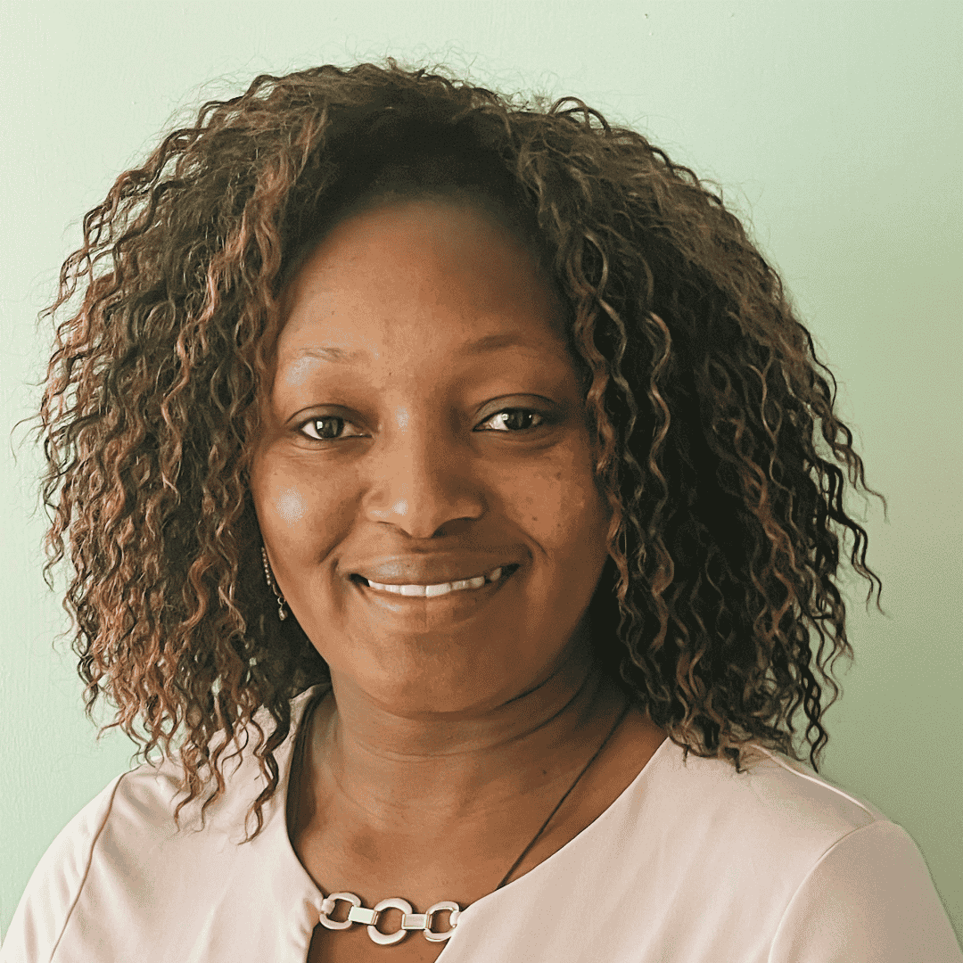 A smiling woman with curly highlighted hair wears a blush pink top and a gold necklace, photographed against a soft green background | ReEvolve Therapy