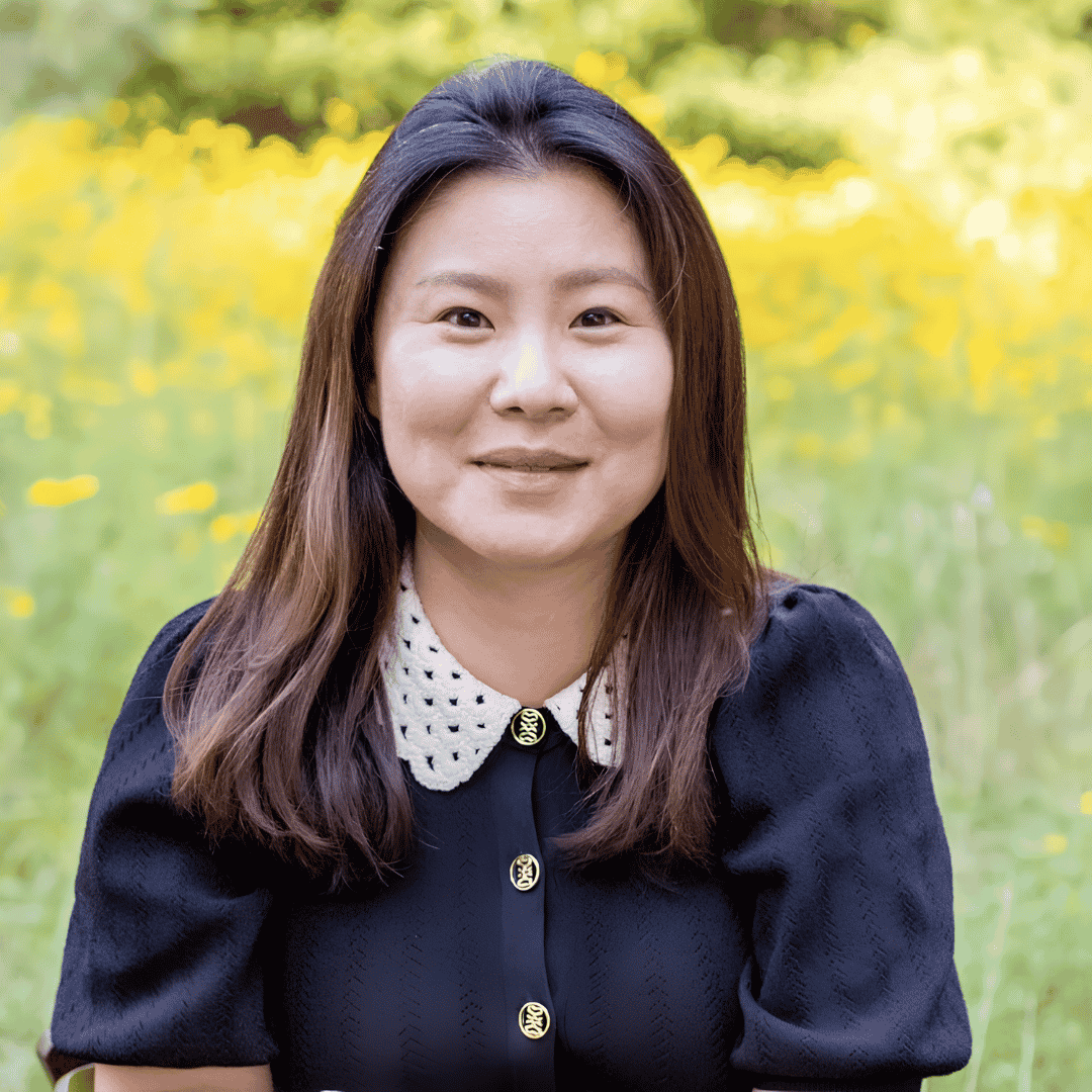 A smiling woman with long dark hair wears a navy top with a crocheted collar, standing in a wildflower field | ReEvolve Therapy