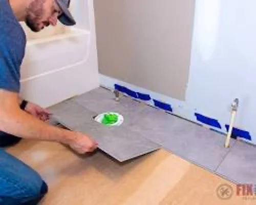 A man installing tile flooring in a room, kneeling on the floor and placing a tile down.