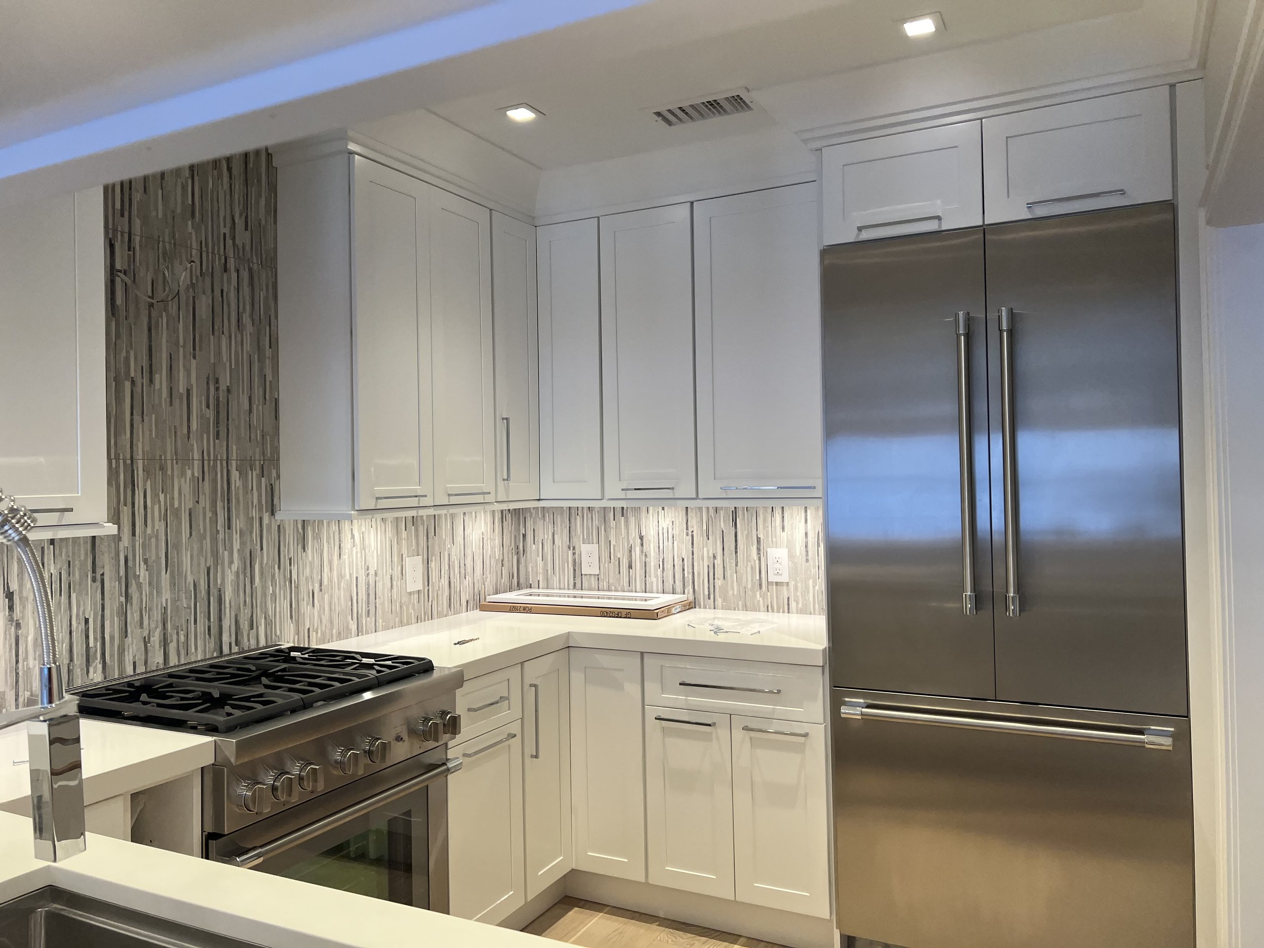 Modern kitchen with white cabinetry, a gray patterned backsplash, stainless steel appliances including a large refrigerator, and a countertop with a stove and oven.