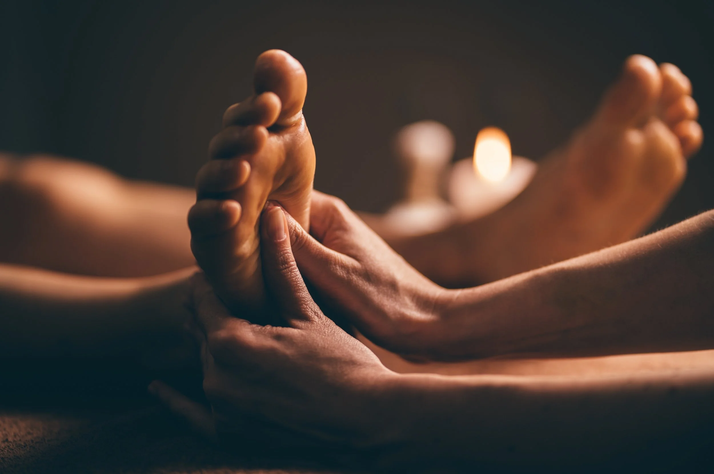 Foot massage in a dimly-lit spa environment with blurred candle in background.