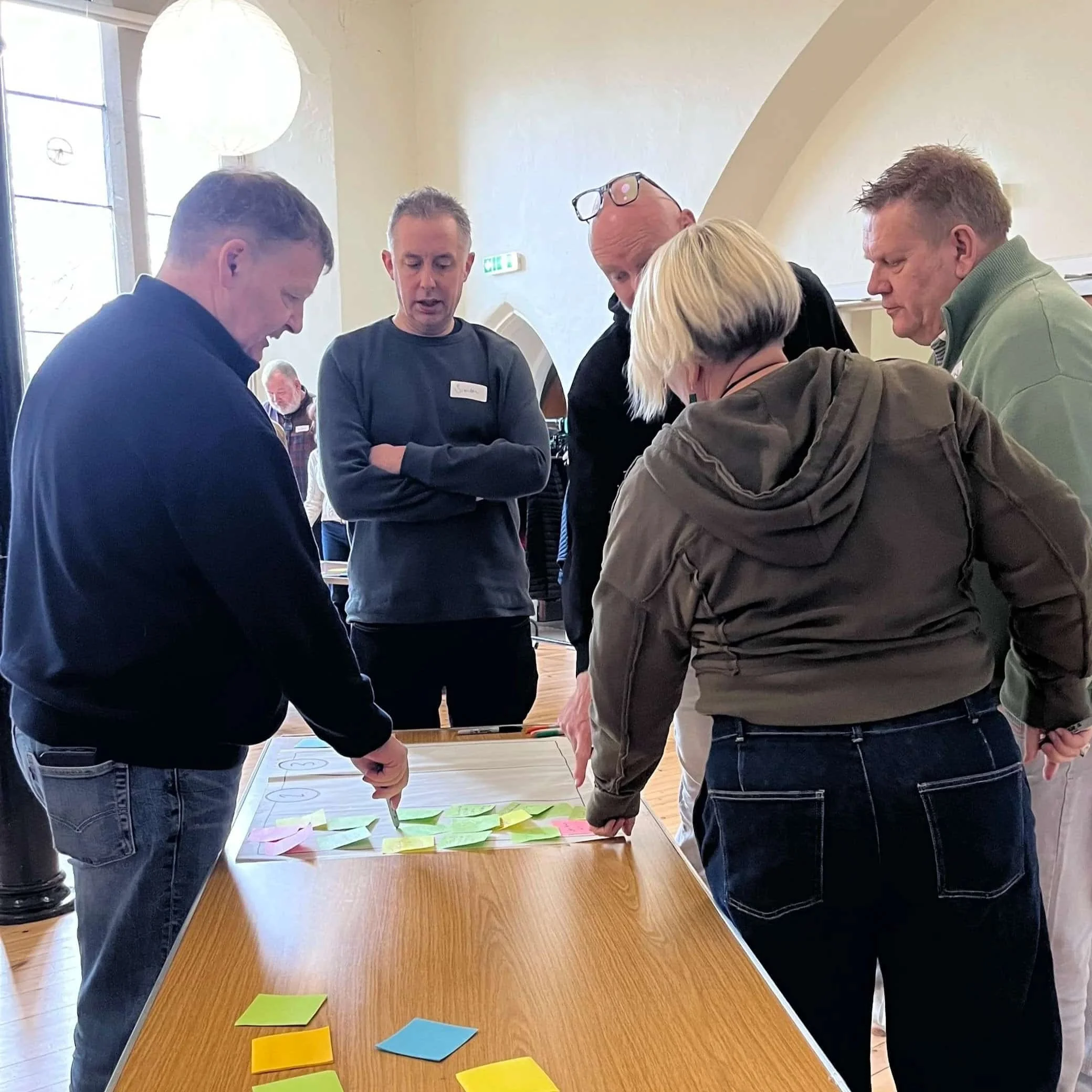 Small group collaborates around a table covered with sticky notes during a workshop.
