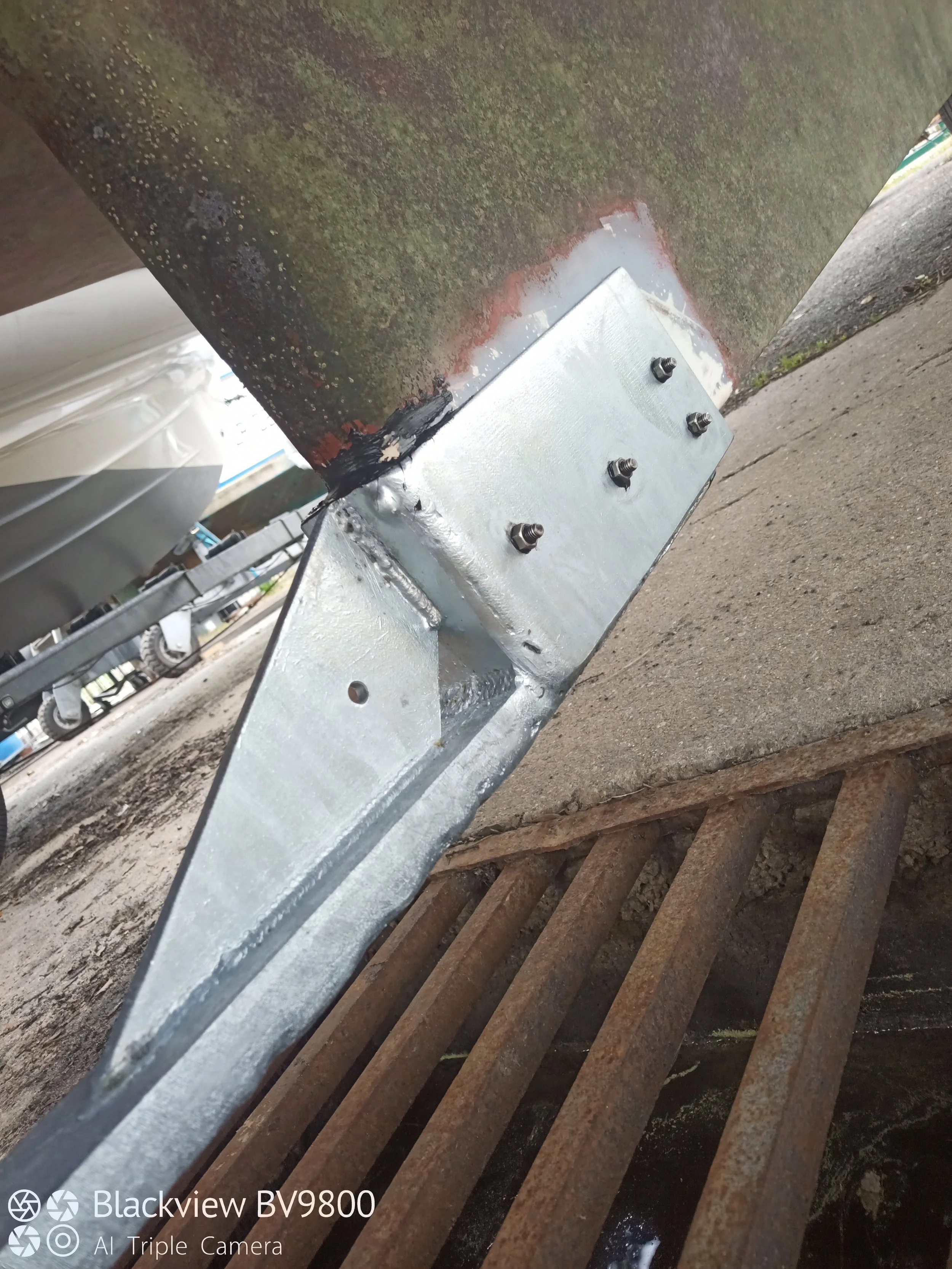 Une charpente métallique avec un support boulonné et une grille en métal rouillée à proximité.