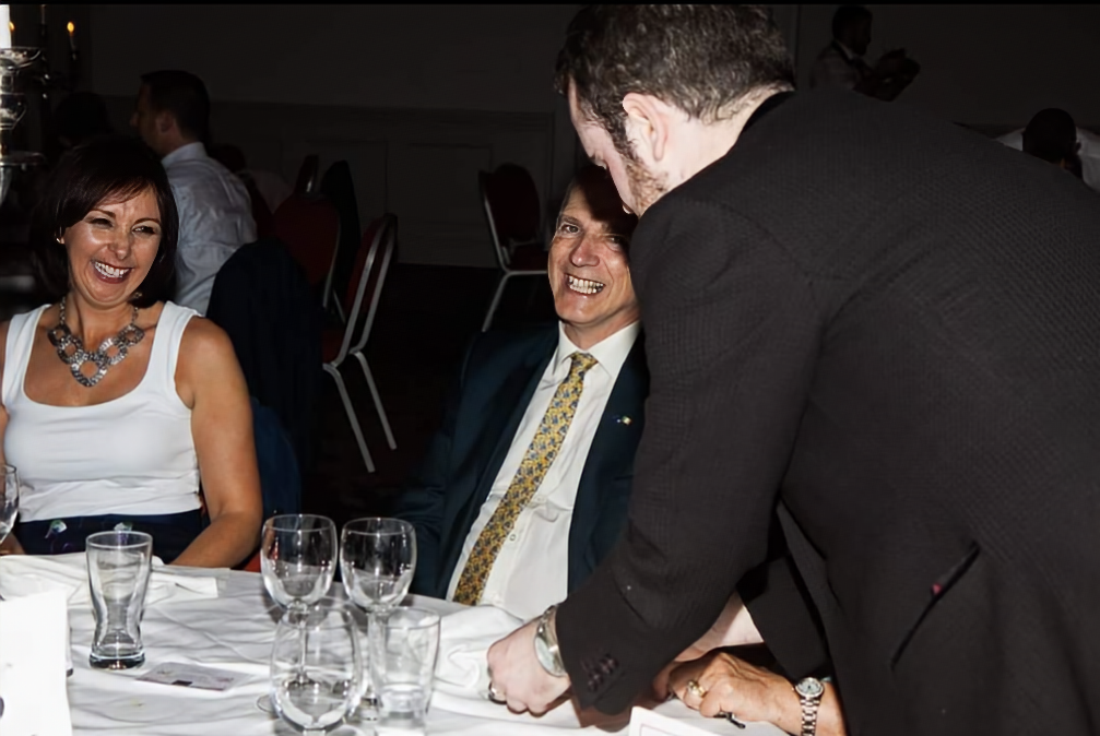 People laughing at a banquet table with David Peace