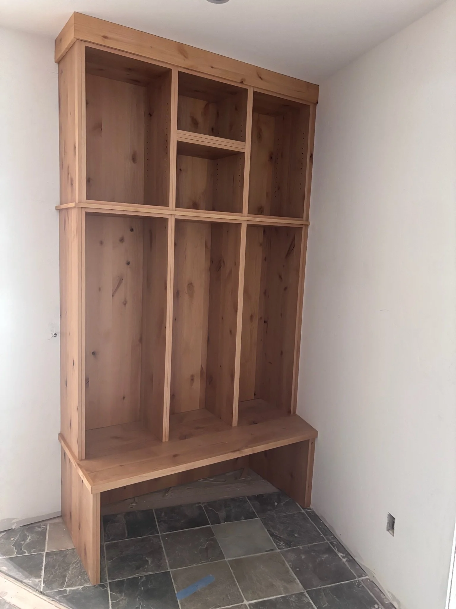 unfinished wooden built-in shelving unit with cabinet space at the bottom, placed against white walls and tile flooring.