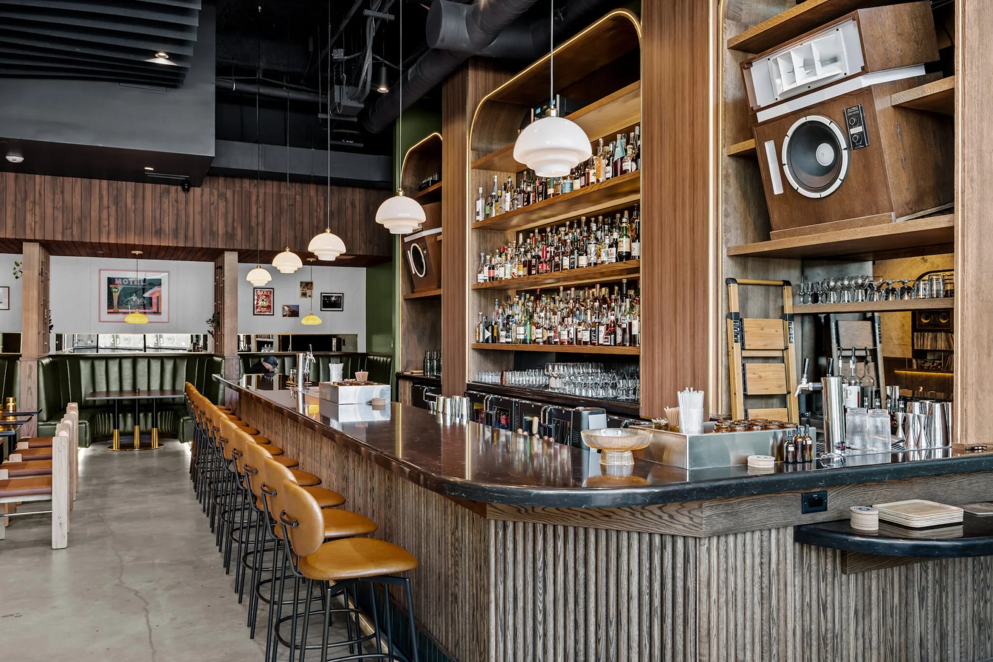 Modern bar with wooden shelves stocked with bottles, bar counter with stools, and contemporary lighting fixtures in the restaurant.