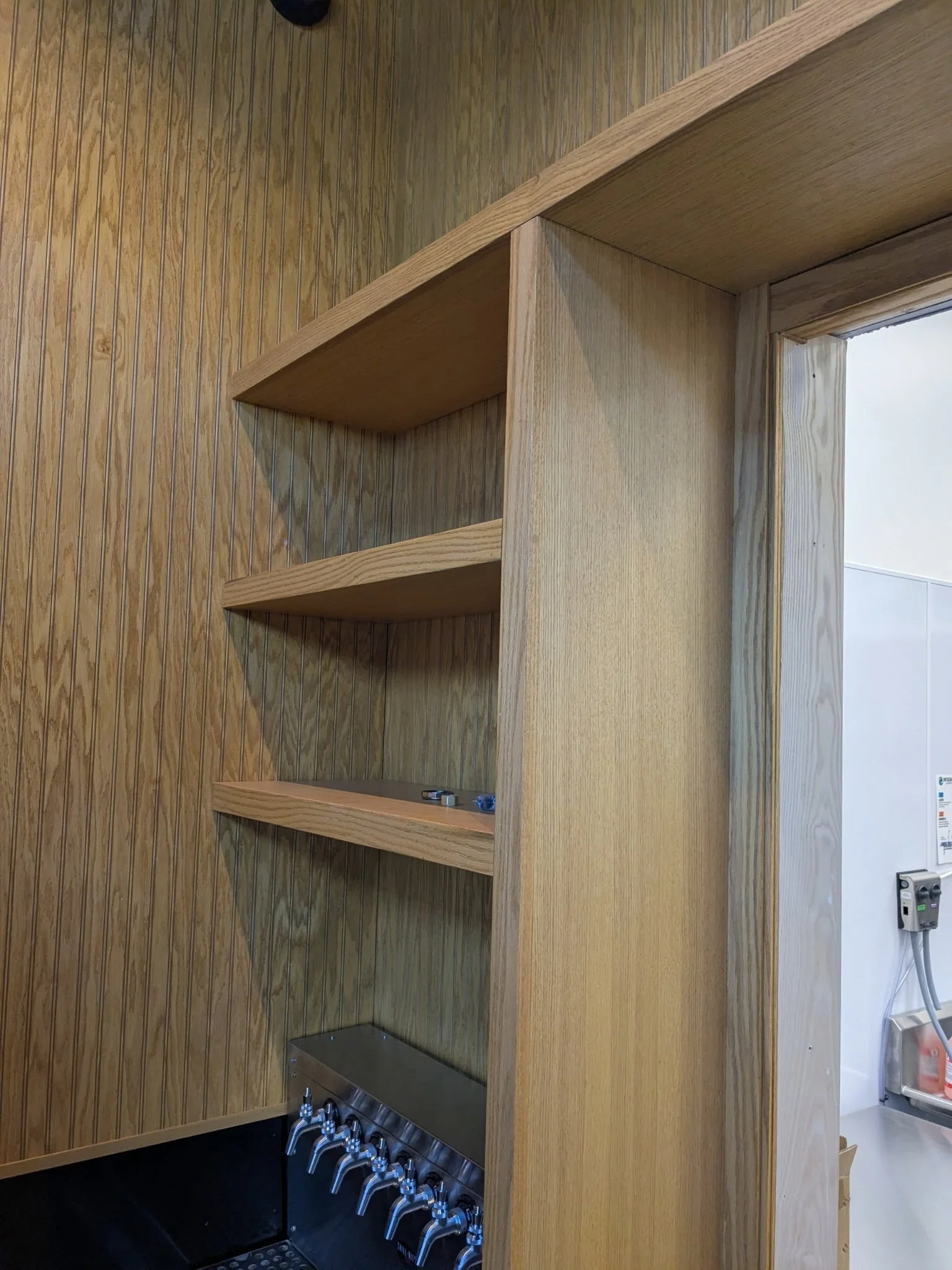 Wooden shelves and a beer tap station in a room with wood paneling.