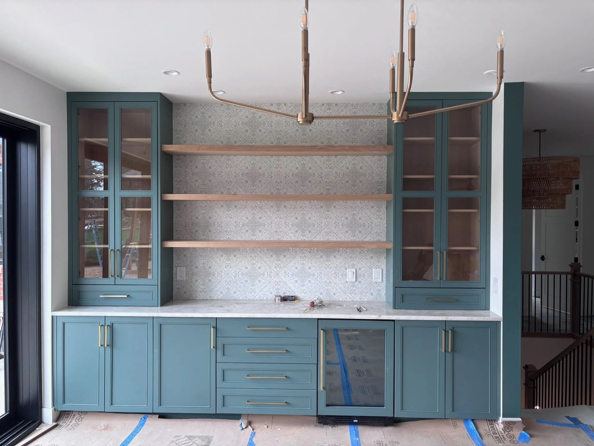 Photo of a new kitchen with green cabinets, light wood open shelves, and a modern chandelier hanging above.