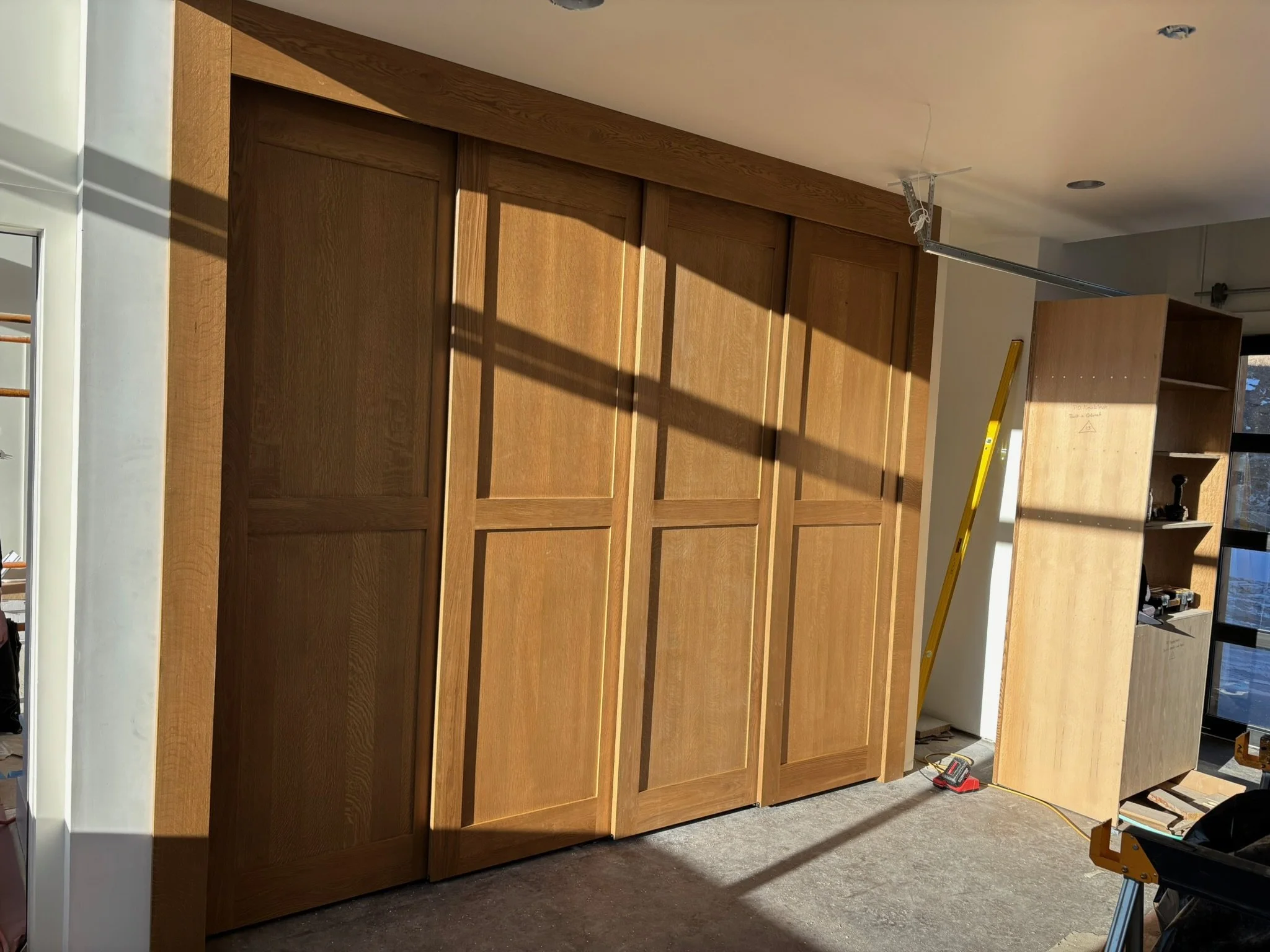 Room with wooden sliding closet doors, a yellow ladder, and construction tools.