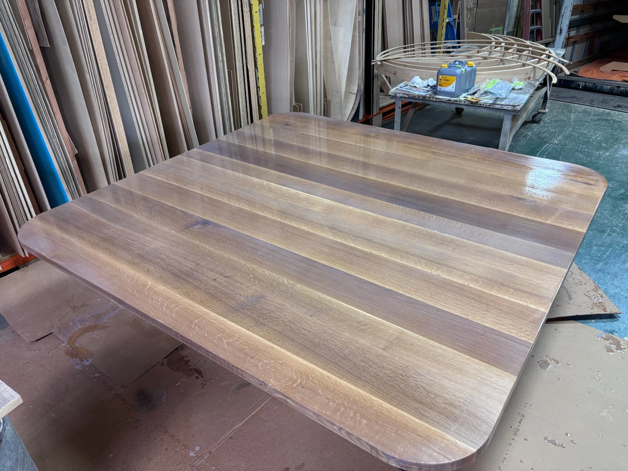 A large wooden table in a workshop surrounded by woodworking materials and tools.