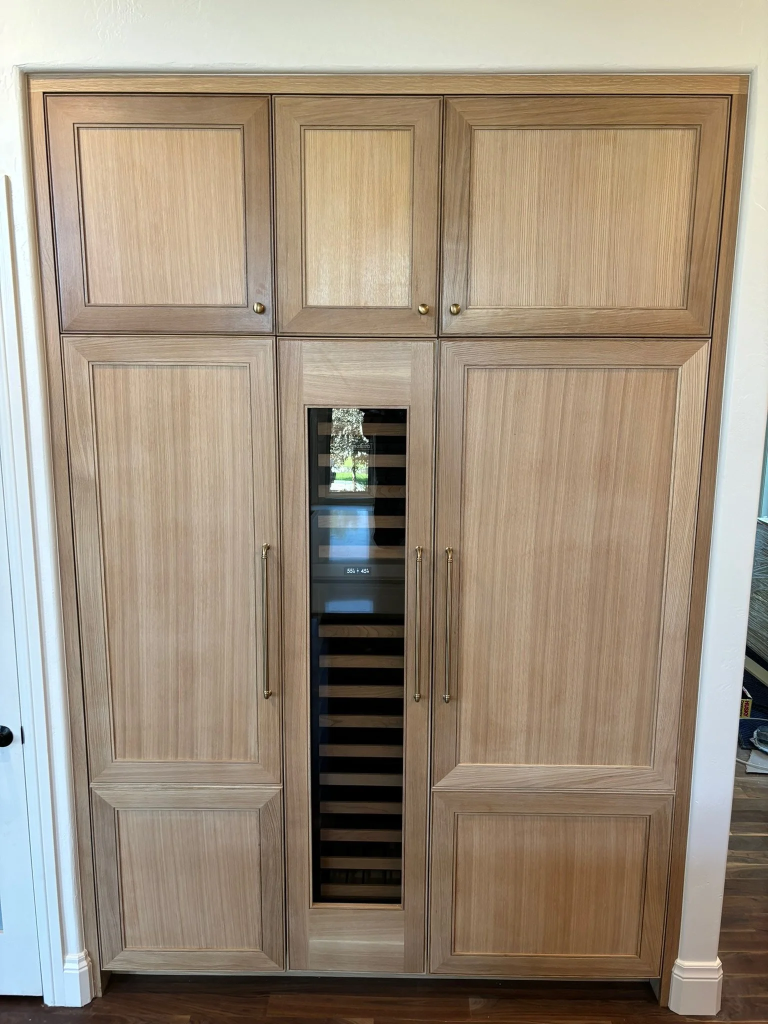 Wooden kitchen cabinet with a built-in wine cooler in the center, featuring glass door and horizontal wooden shelves.