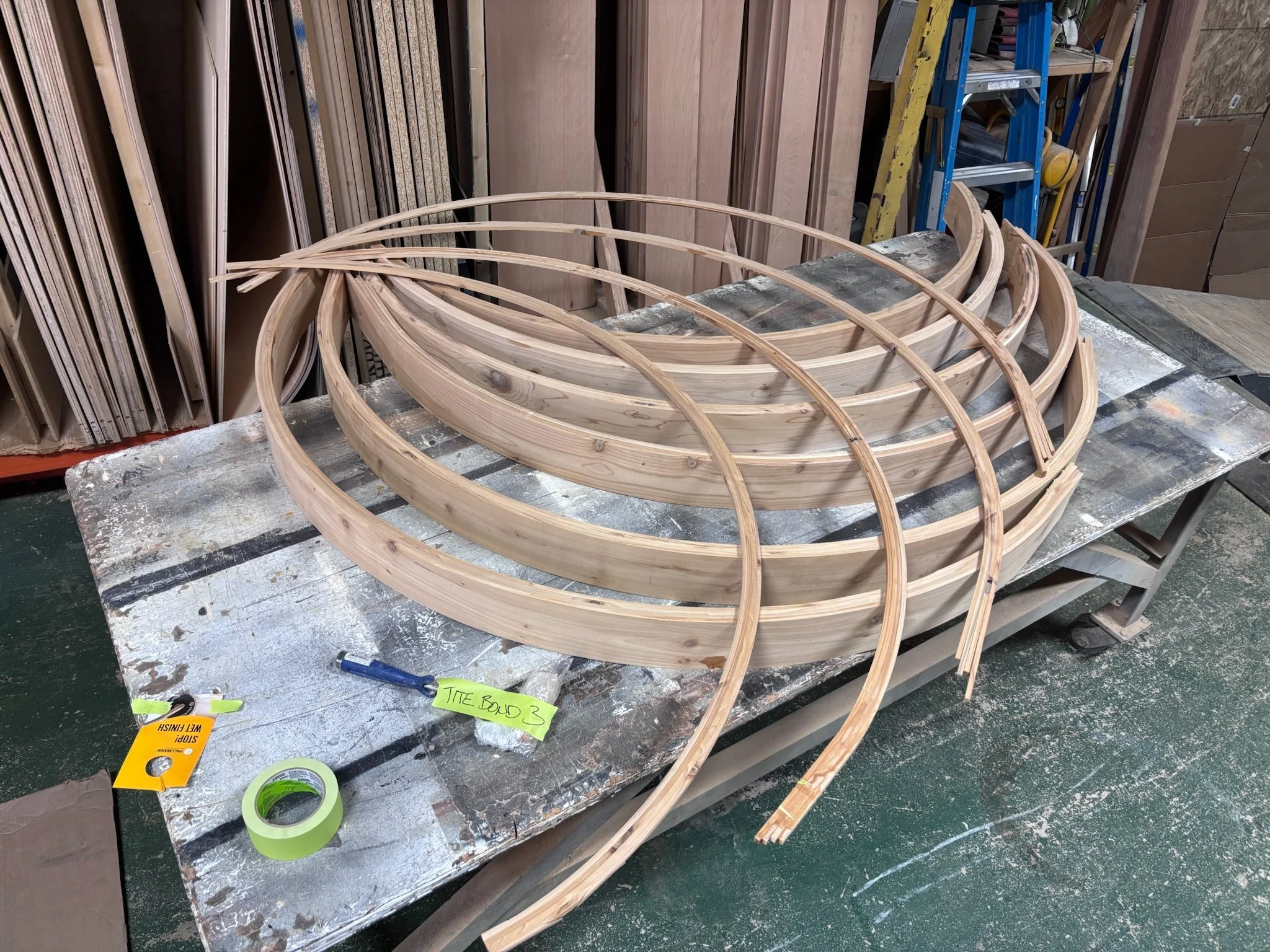 Wooden curved frames on workbench in carpentry workshop with tools and wood storage in background.