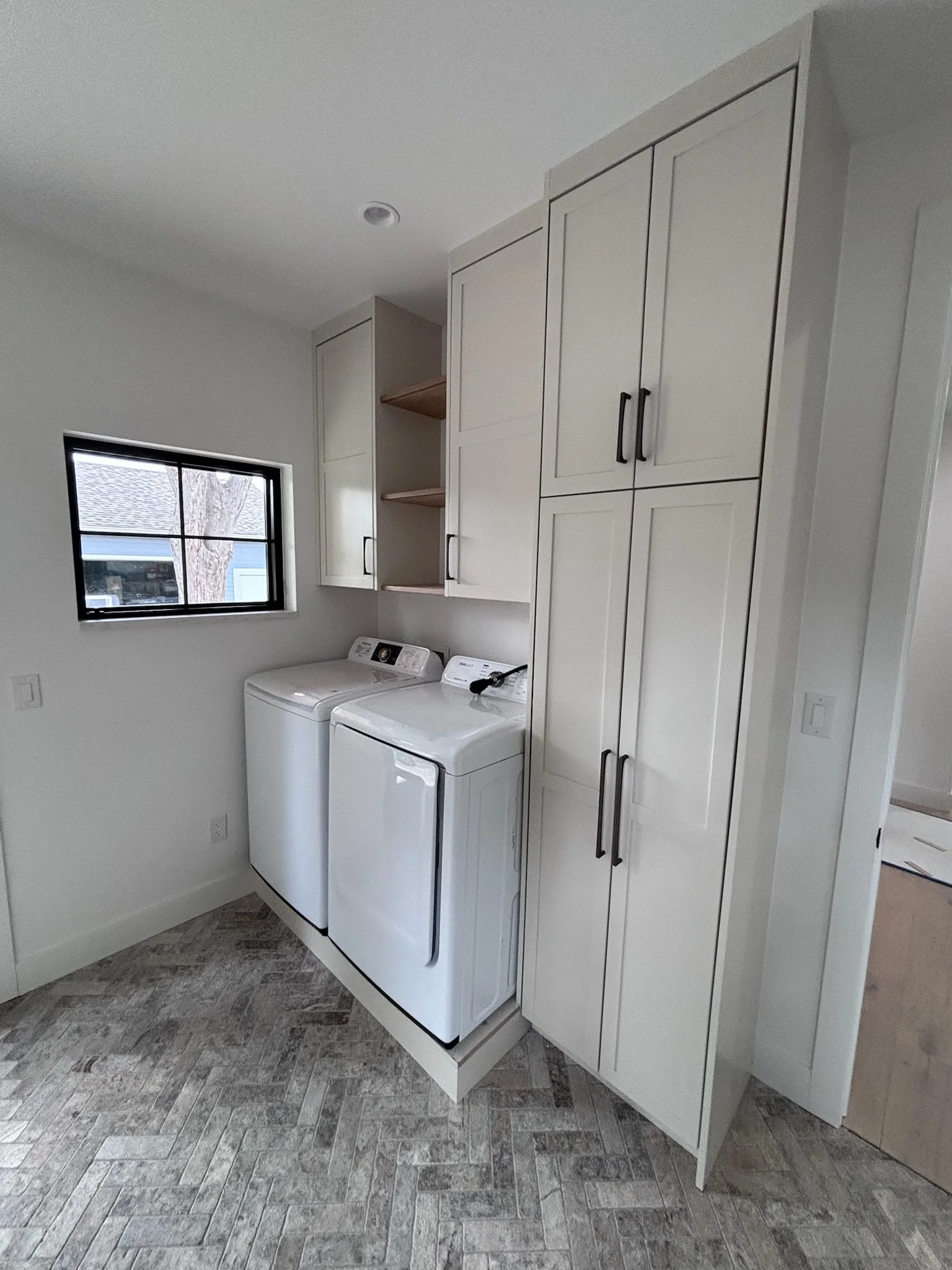 Laundry room with white washing machine and dryer, white cabinets, and a small window.