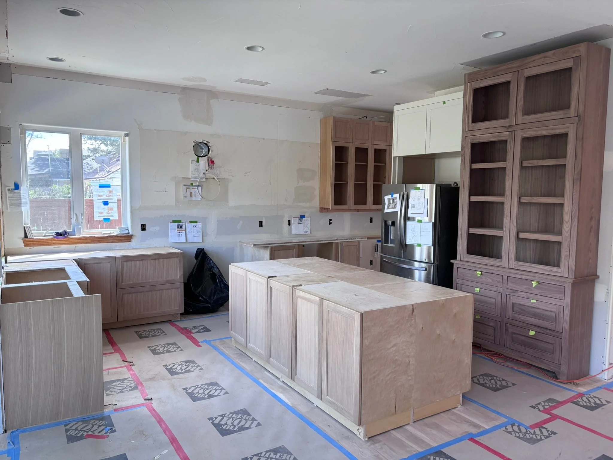 Kitchen under construction with unfinished cabinets, a window, and construction materials on the floor.
