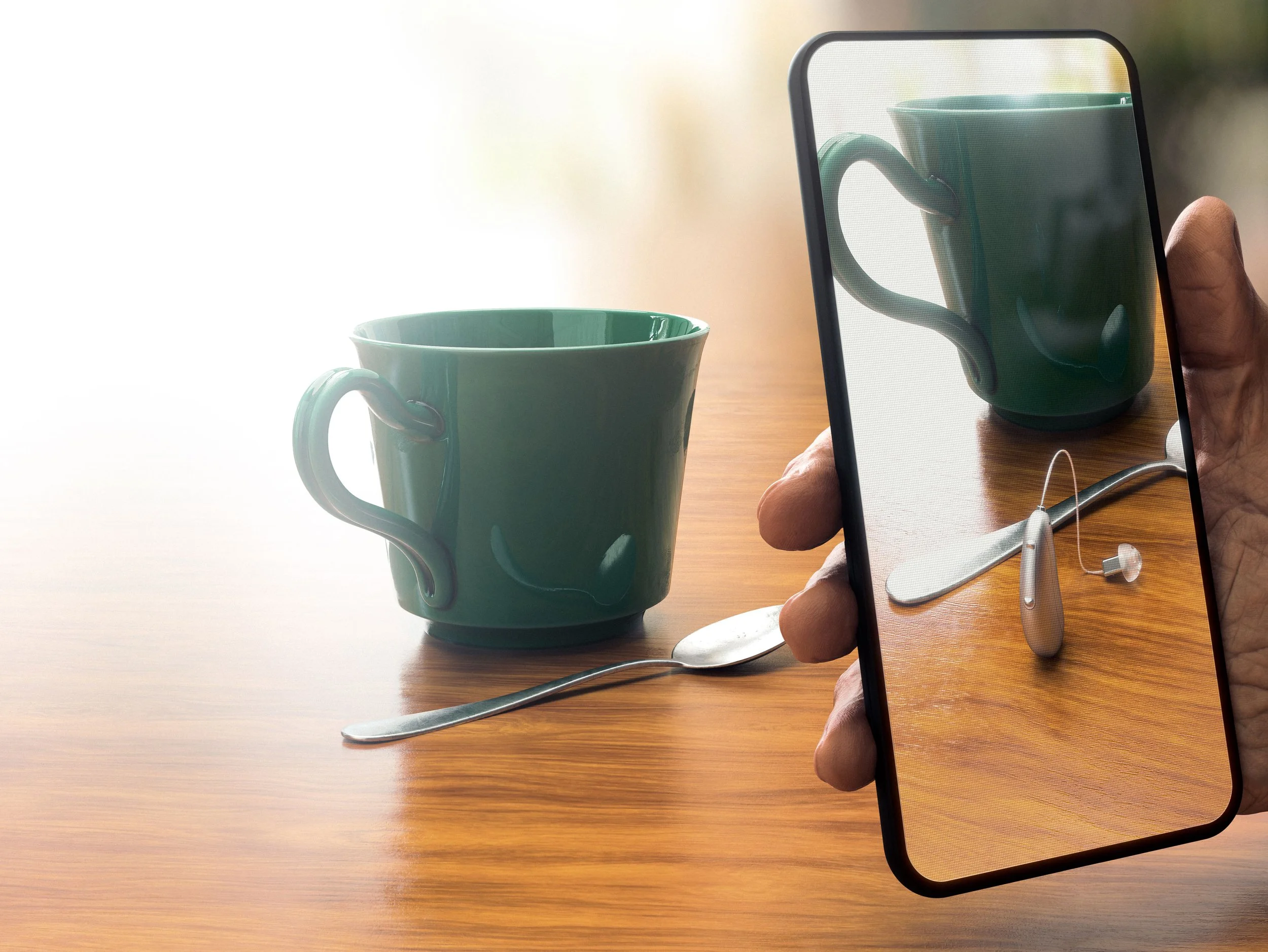A person holding a smartphone taking a photo of a green ceramic mug and a metal spoon on a wooden table.