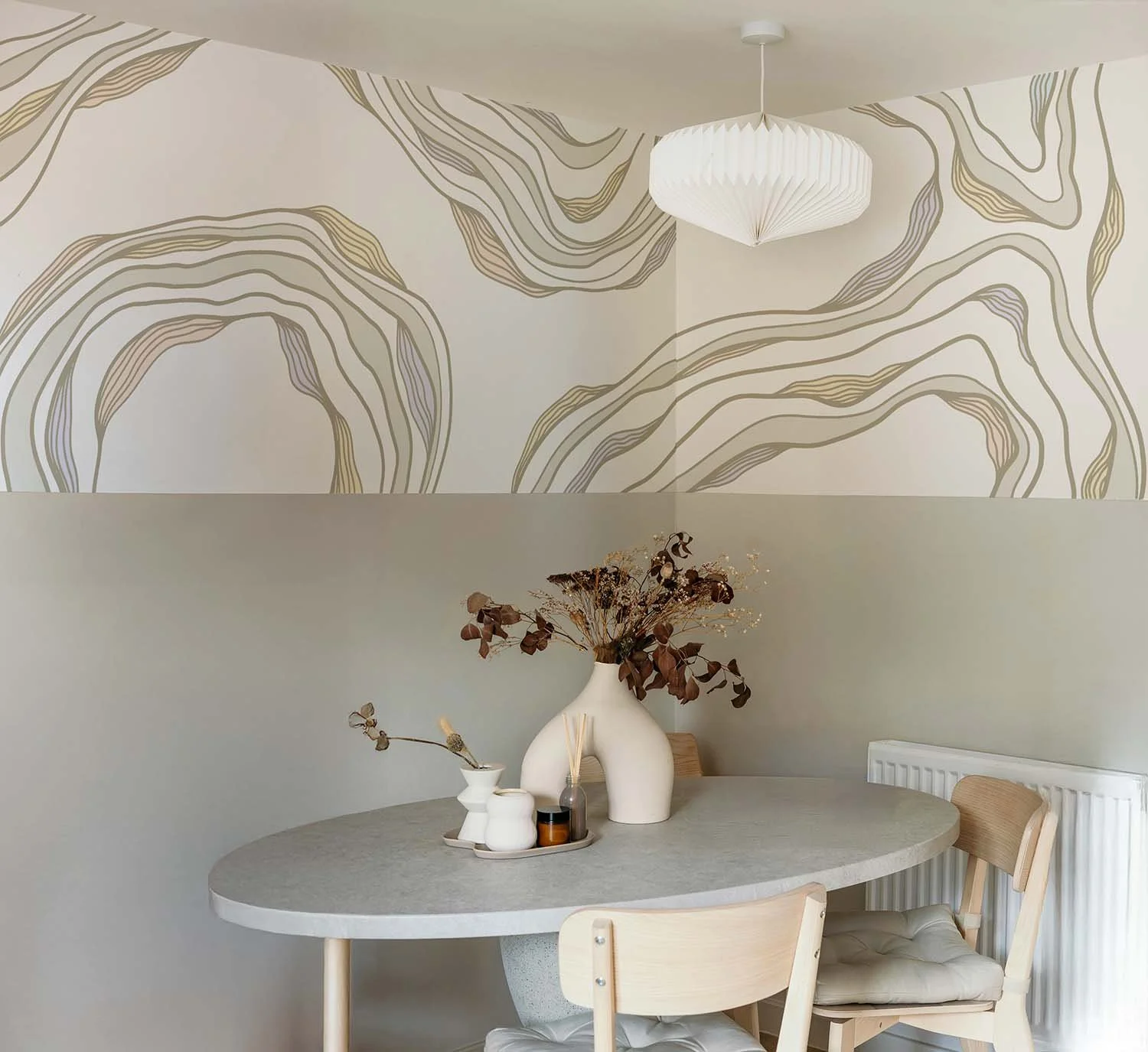 A modern boutique cafe dining area with a round table, wooden chairs, and a large white vase with dried flowers. Above is a hand painted custom wall mural of organic neutral toned flowing lines and shapes. SF Bay Area mural artist portfolio.