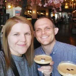 A smiling woman and man holding coffee cups in a cozy cafe with cherry blossom decorations.