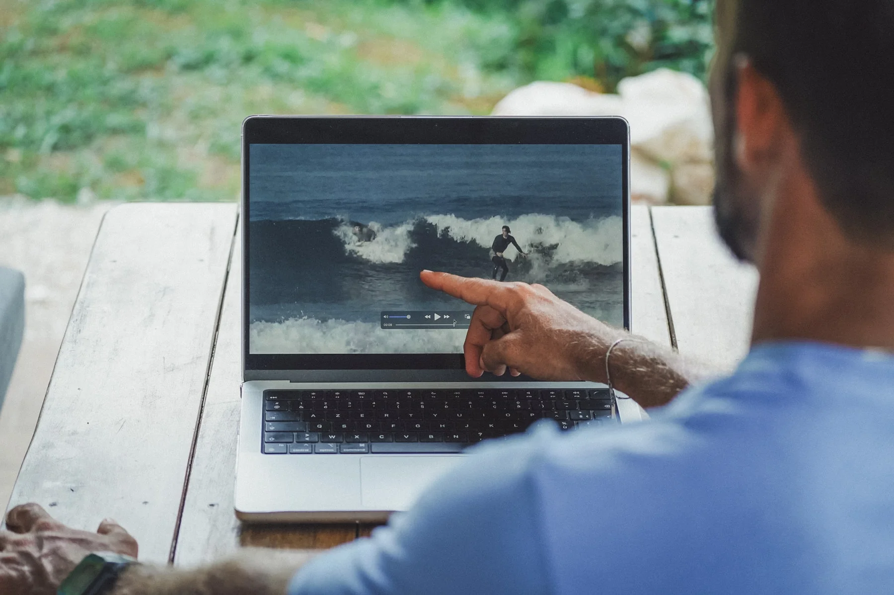Surf coach reviewing video analysis footage with a student on a laptop outdoors in Costa Rica, pointing at surfing technique on screen.