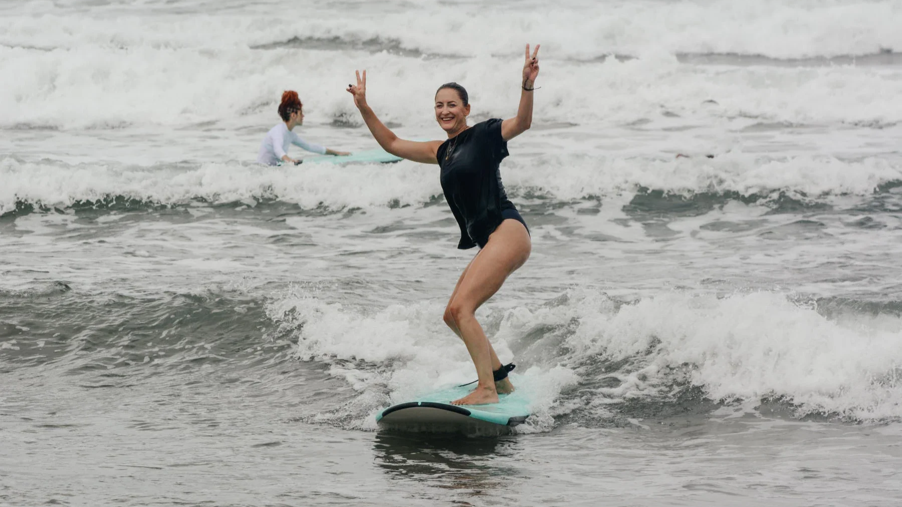 Woman smiling while riding a wave during a surf lesson at Playa Guiones Nosara Costa Rica, another surfer in the background.