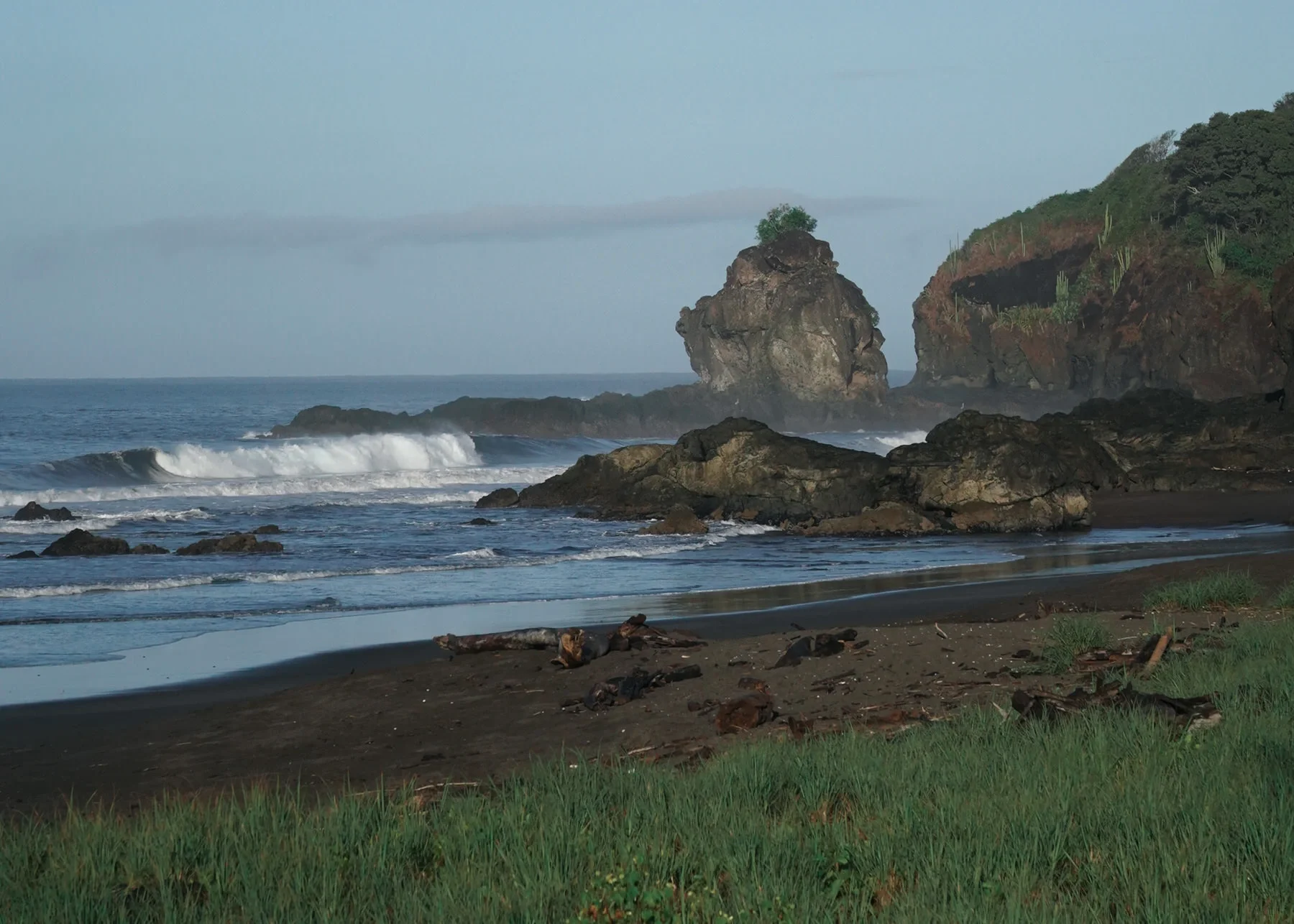 Rugged coastline at Playa Ostional Costa Rica with rocky cliffs, waves crashing on the shore and driftwood on the sandy beach, a unique surfing destination on the North Pacific coast.