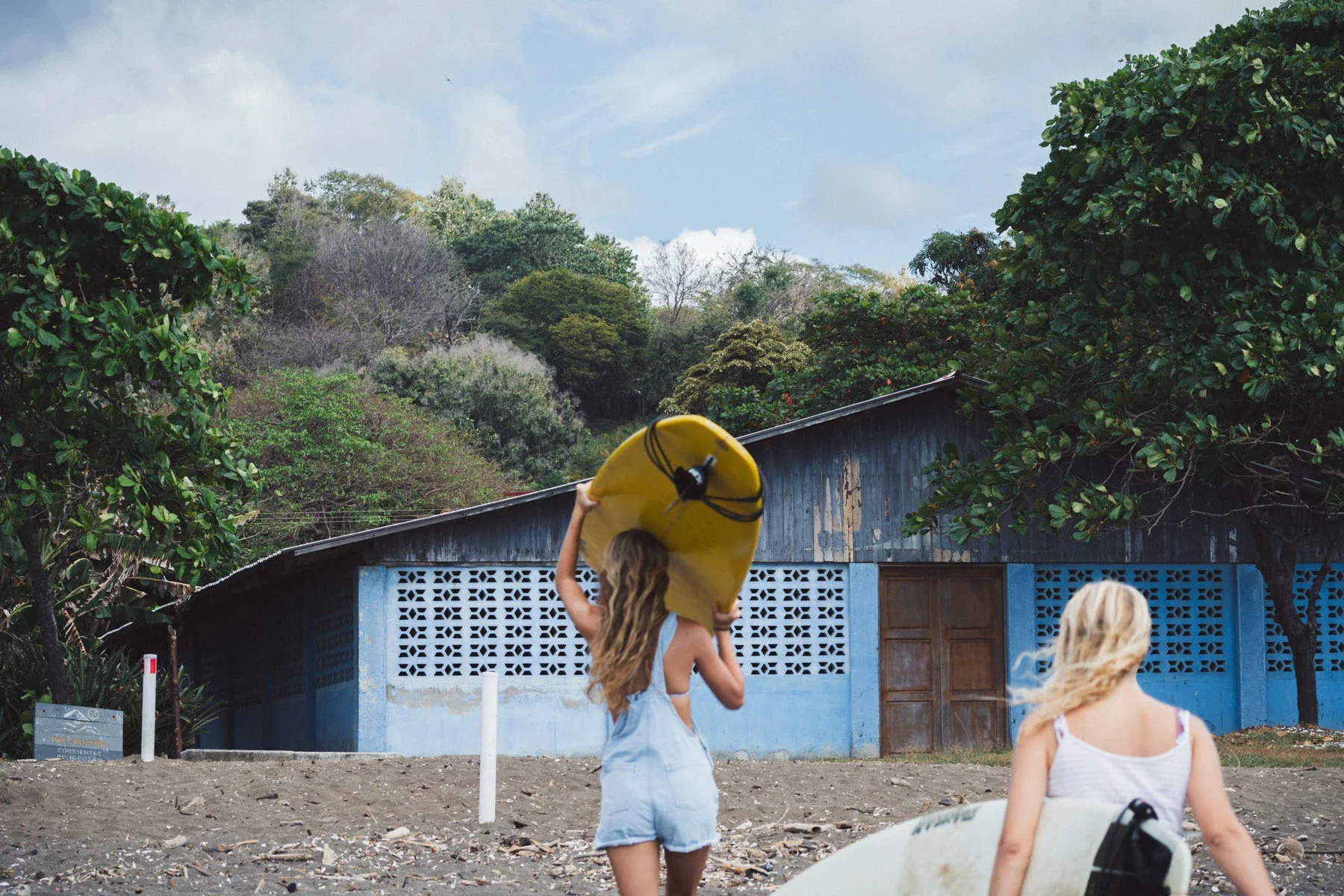 Two surfers carrying surfboards on the beach at Playa Ostional during a surf trip in Costa Rica, lush green trees in the background.
